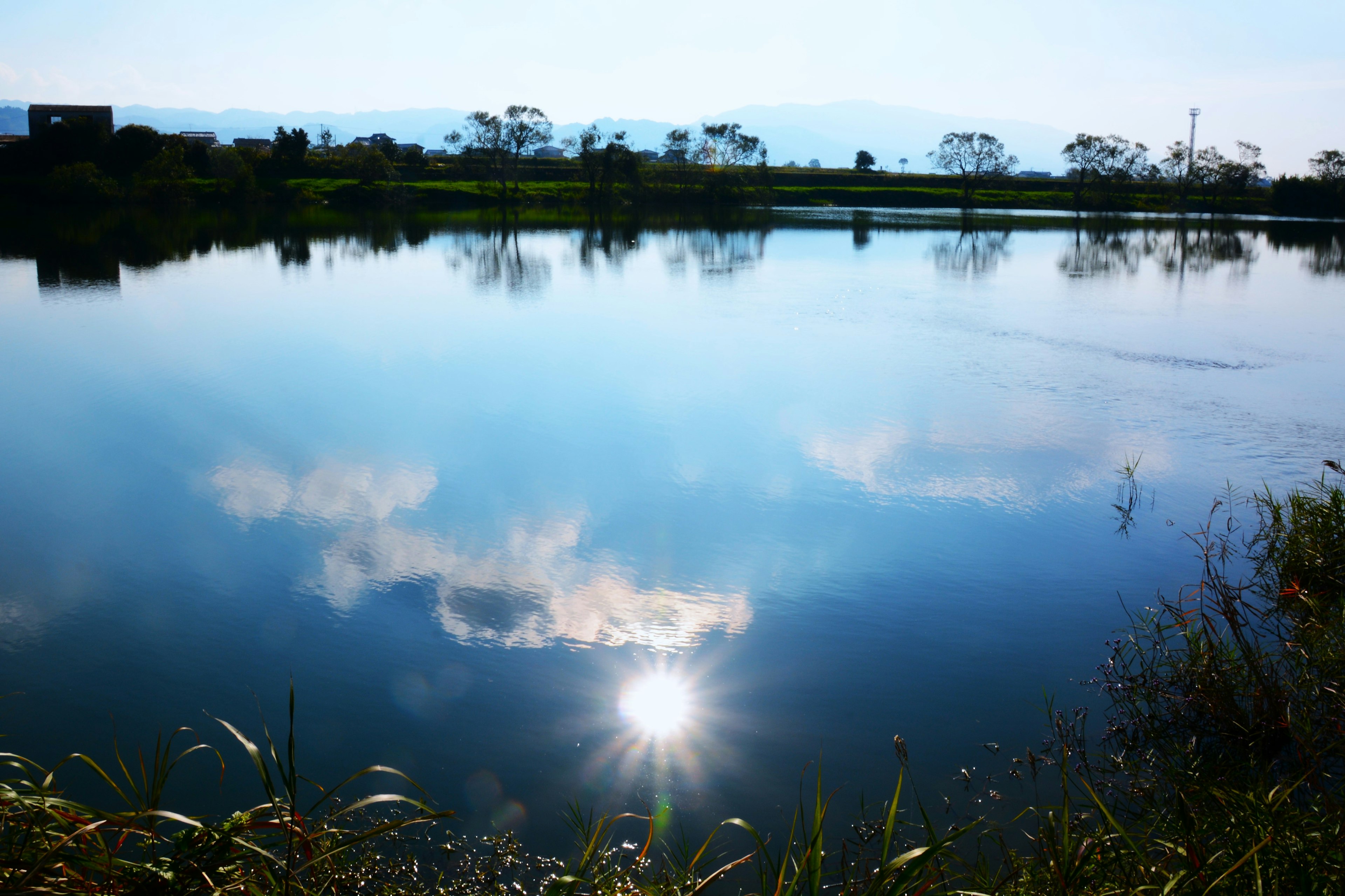 Ruhiger See, der die Sonne und den blauen Himmel spiegelt