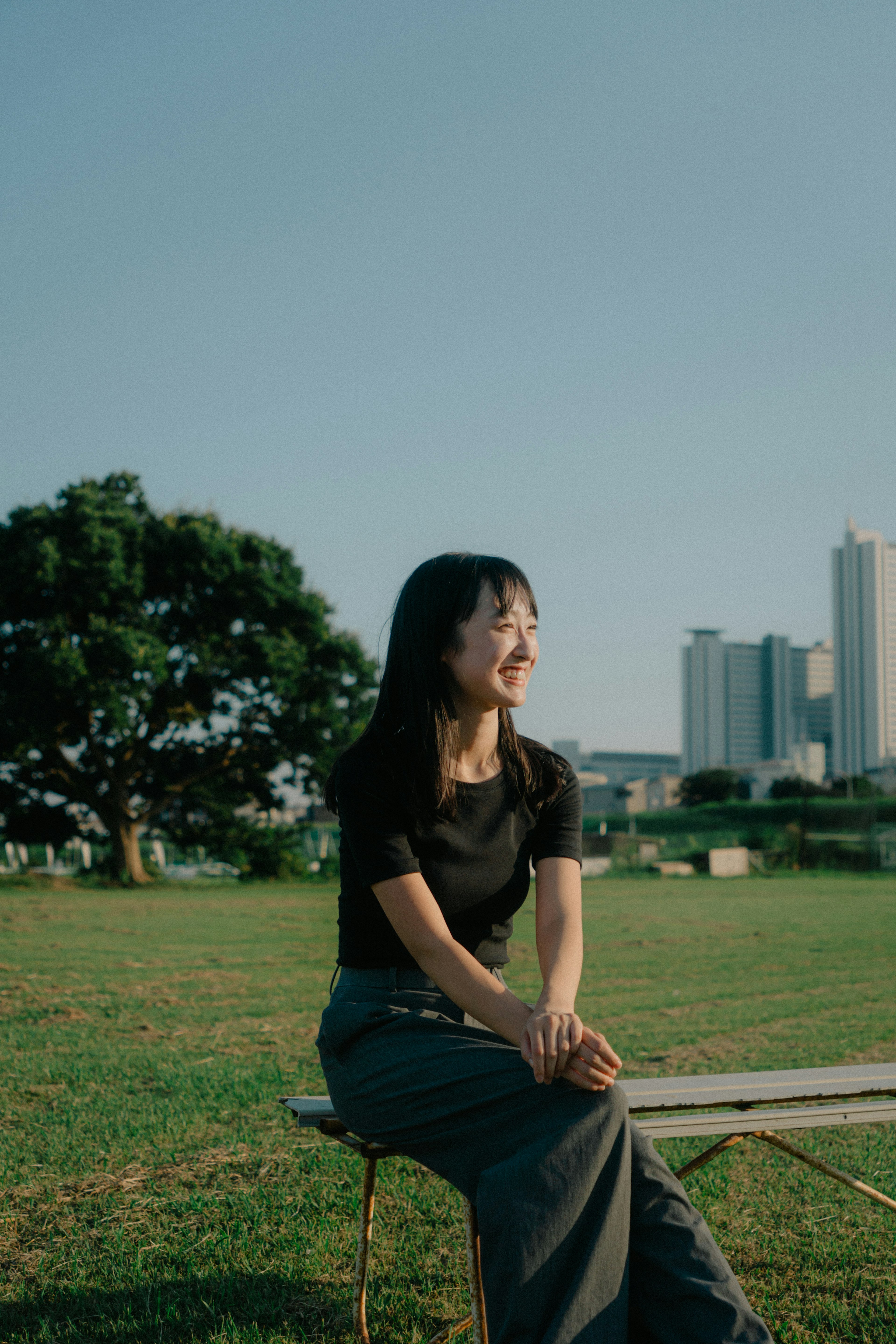 Una mujer sentada en un parque con un horizonte urbano y un gran árbol al fondo