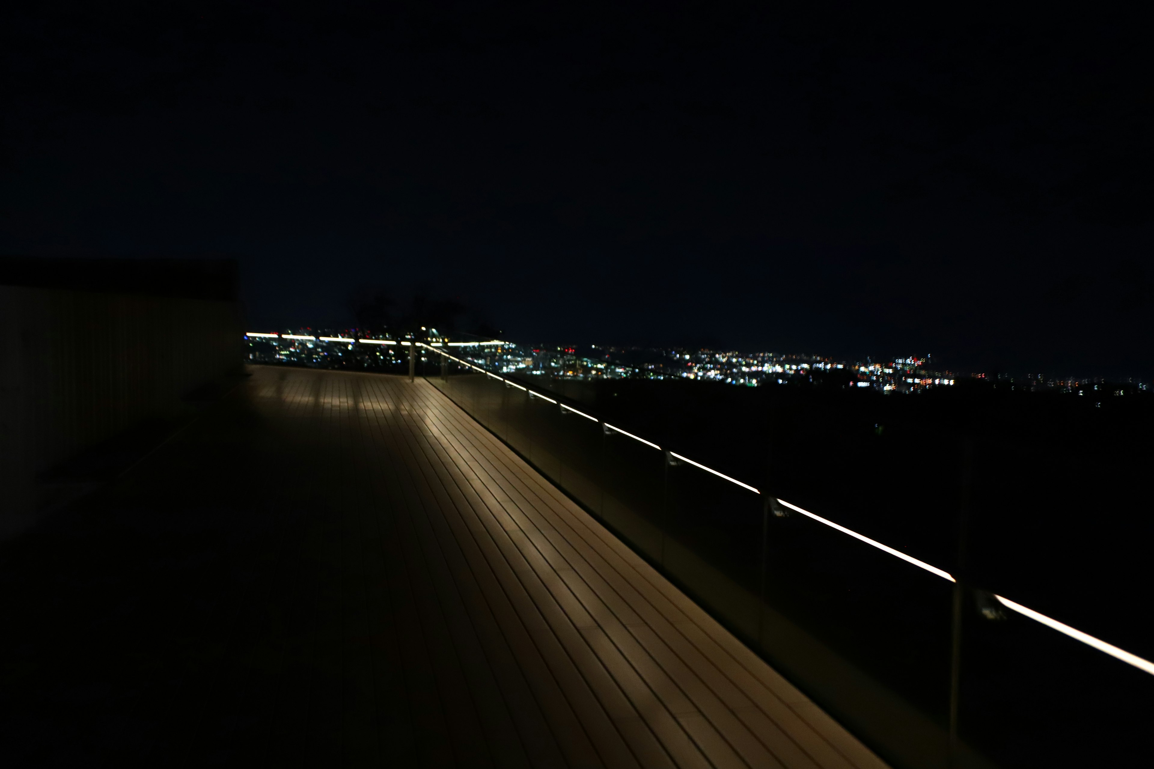 Terrazza in legno con parapetto illuminato che sovrasta una città di notte