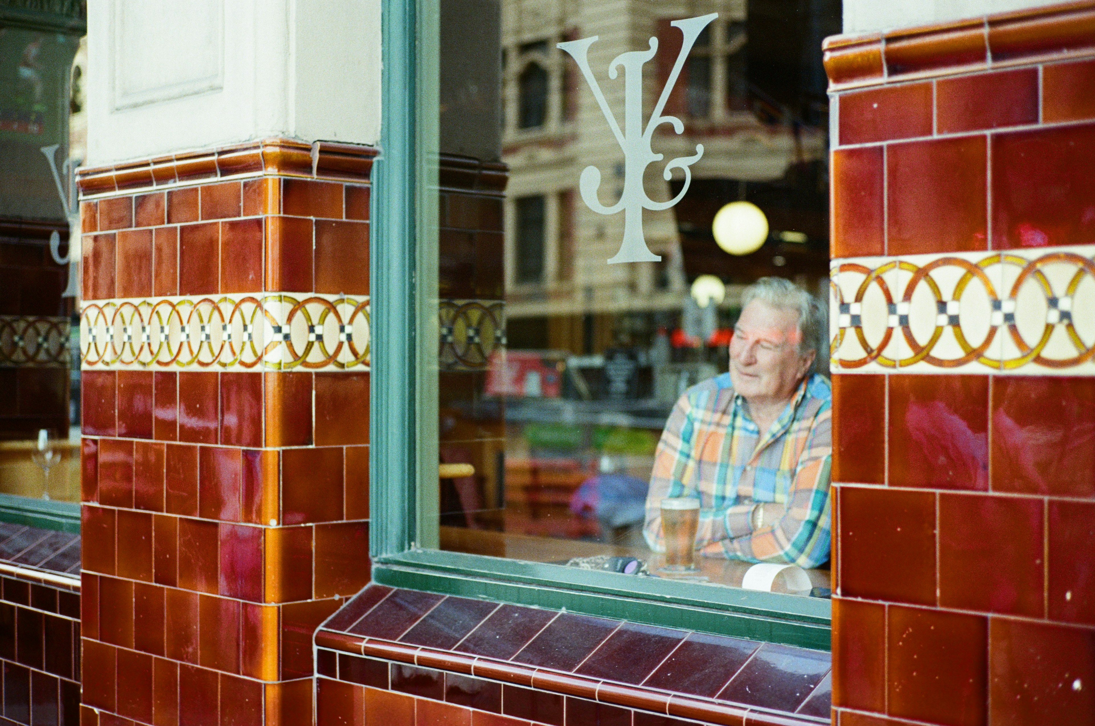 Un hombre disfrutando de una cerveza por la ventana con paredes de azulejos rojos y un logo de la tienda