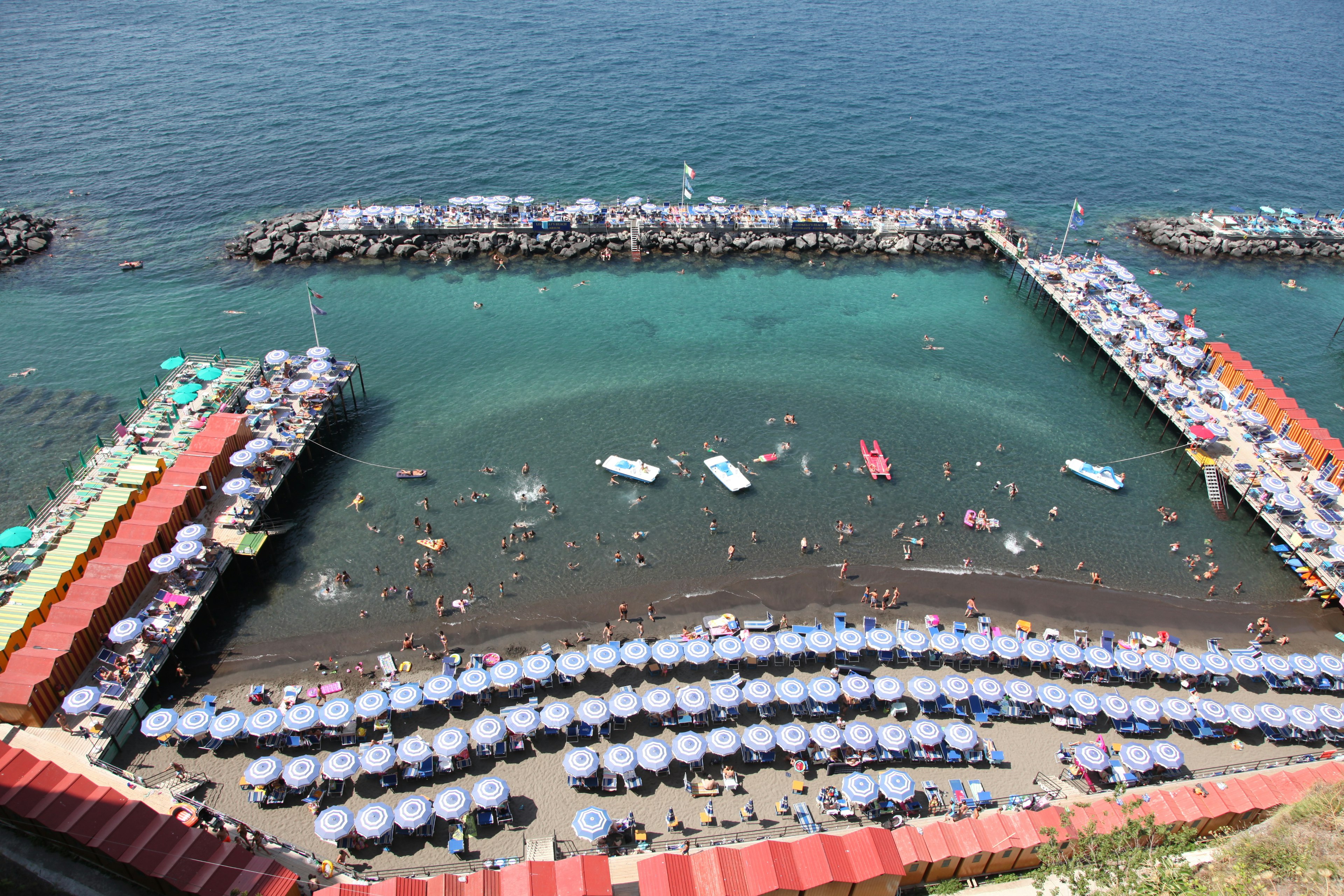 Panoramablick auf einen Strand und das Meer mit zahlreichen Sonnenschirmen und Booten sichtbar