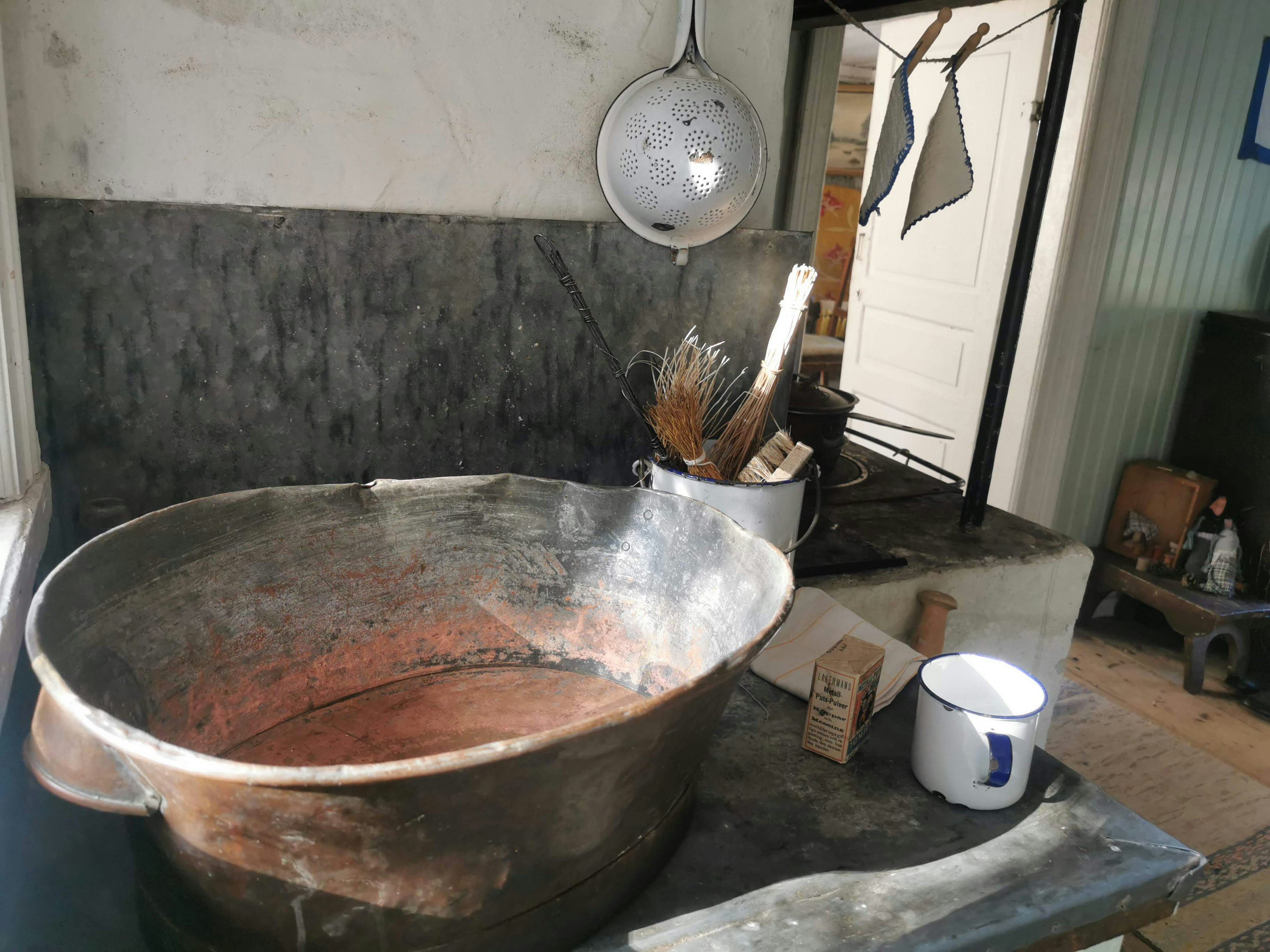 Escena de cocina antigua con utensilios de cocina que incluye una gran olla de cobre y herramientas de madera