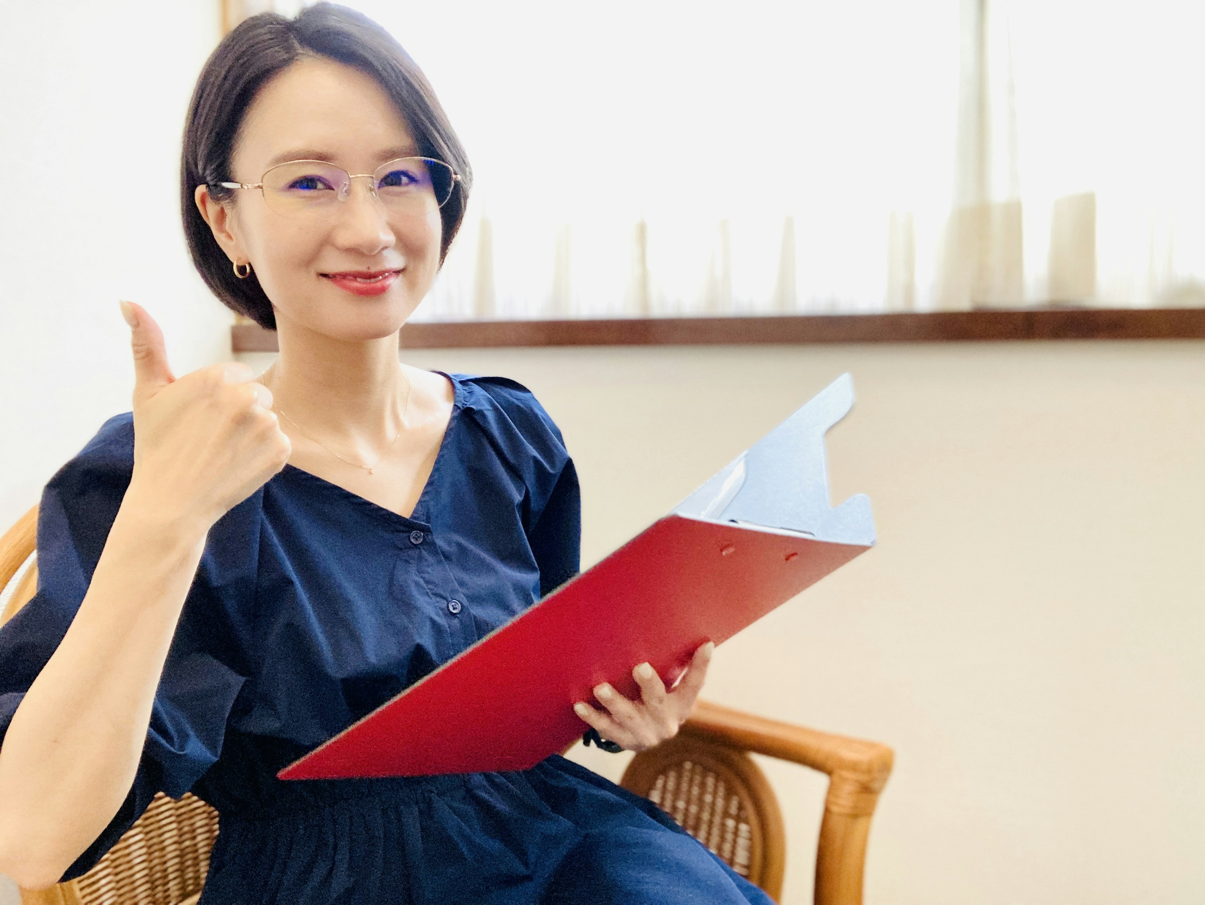 A woman smiling and giving a thumbs up while holding a red folder