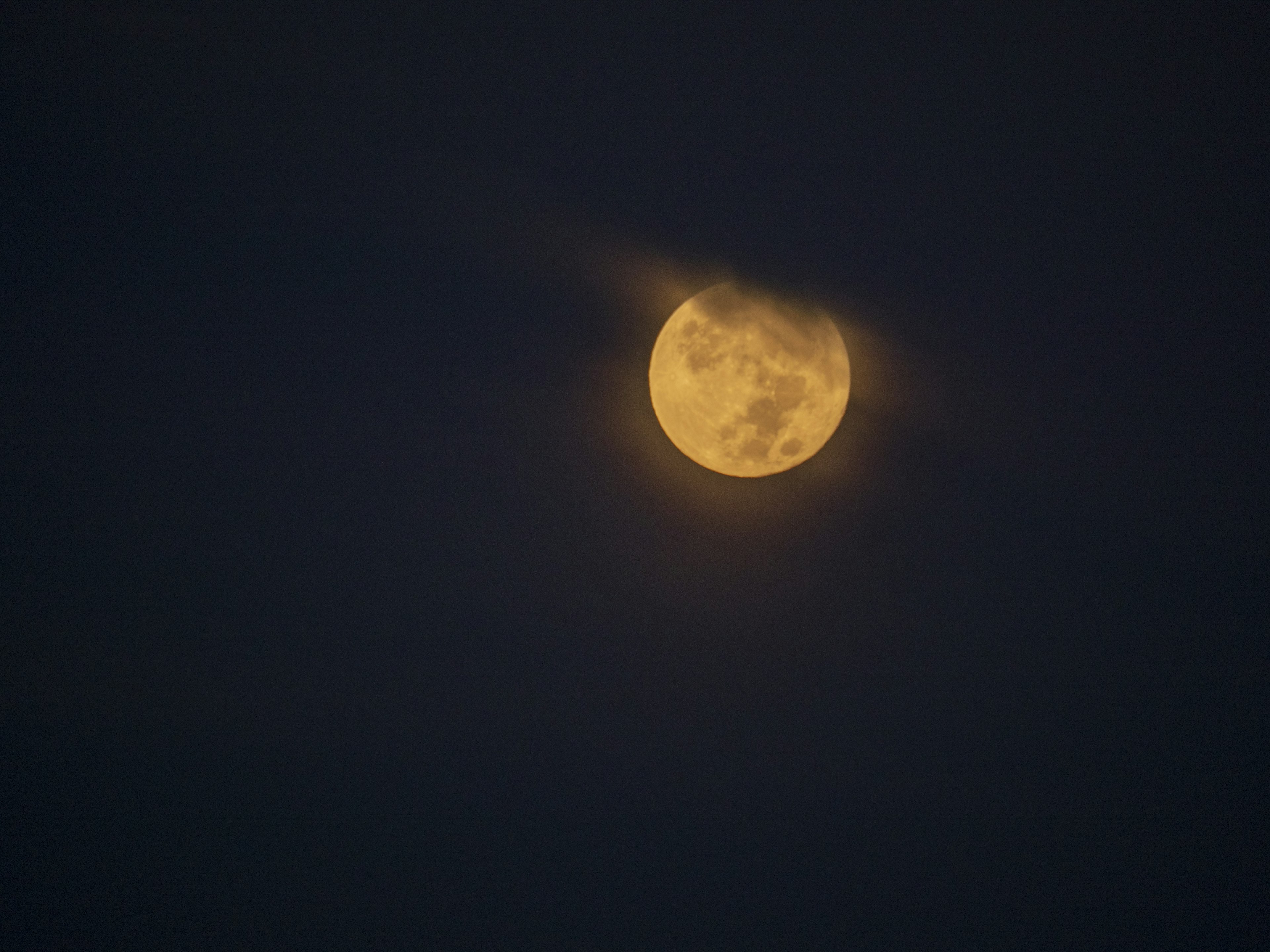 Nahaufnahme eines Vollmonds, teilweise von Wolken verdeckt, vor einem dunklen Himmel