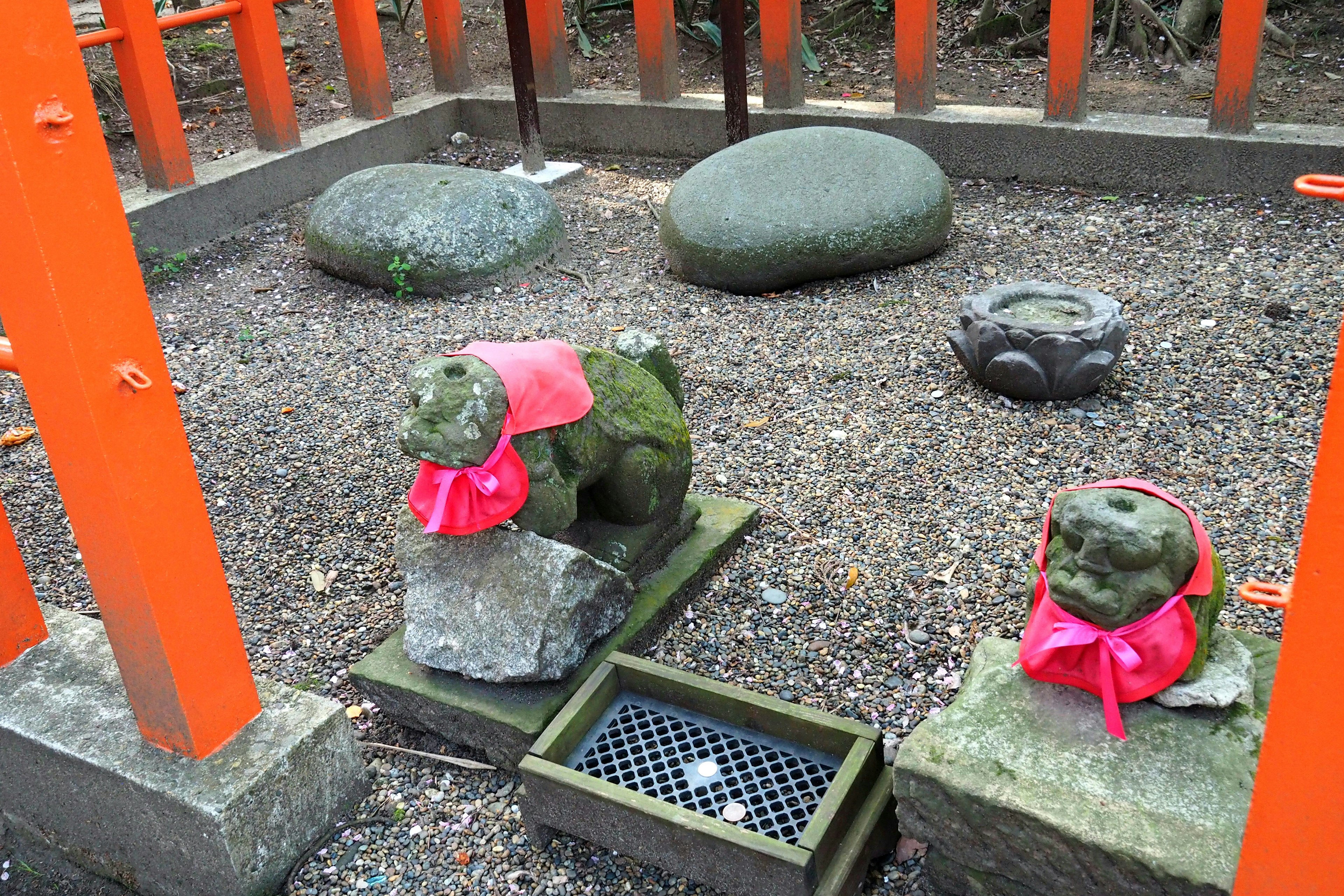 Escena serena en un patio de santuario con estatuas de piedra que llevan bufandas rojas