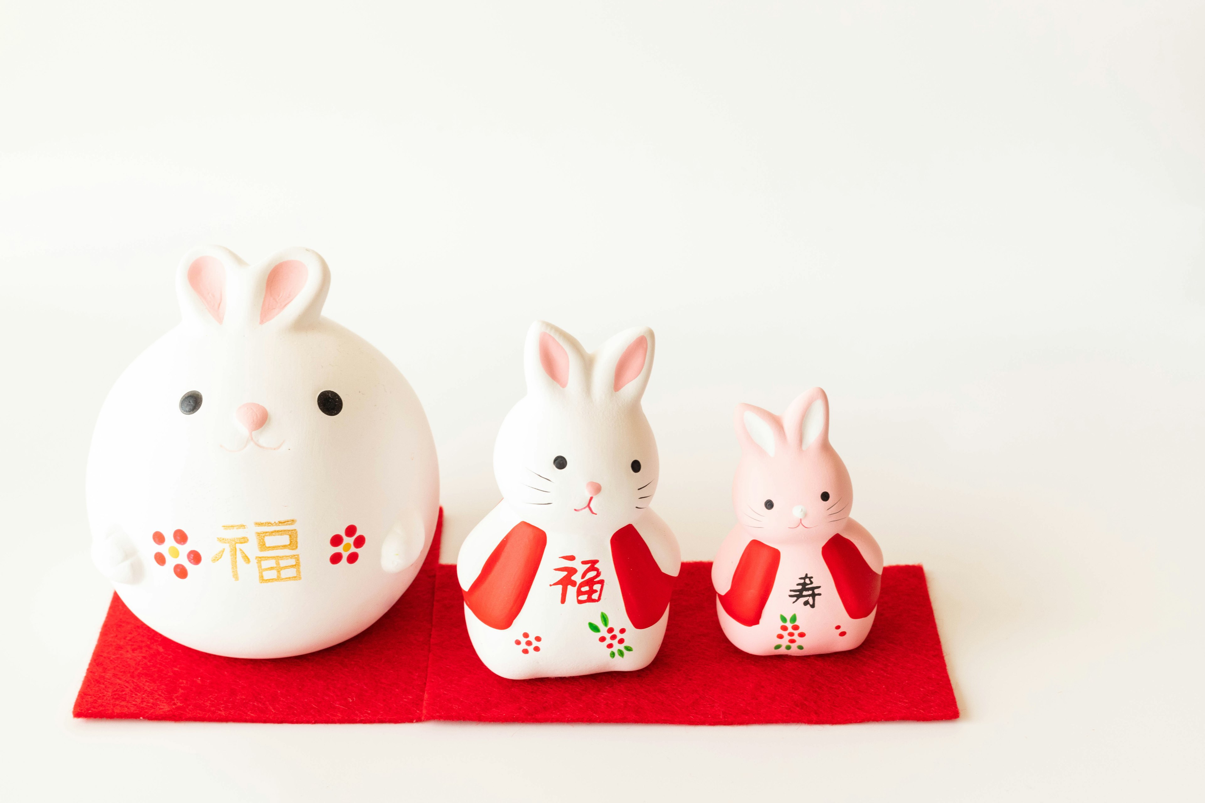 Three rabbit figurines and a large rabbit figure on a red mat against a white background