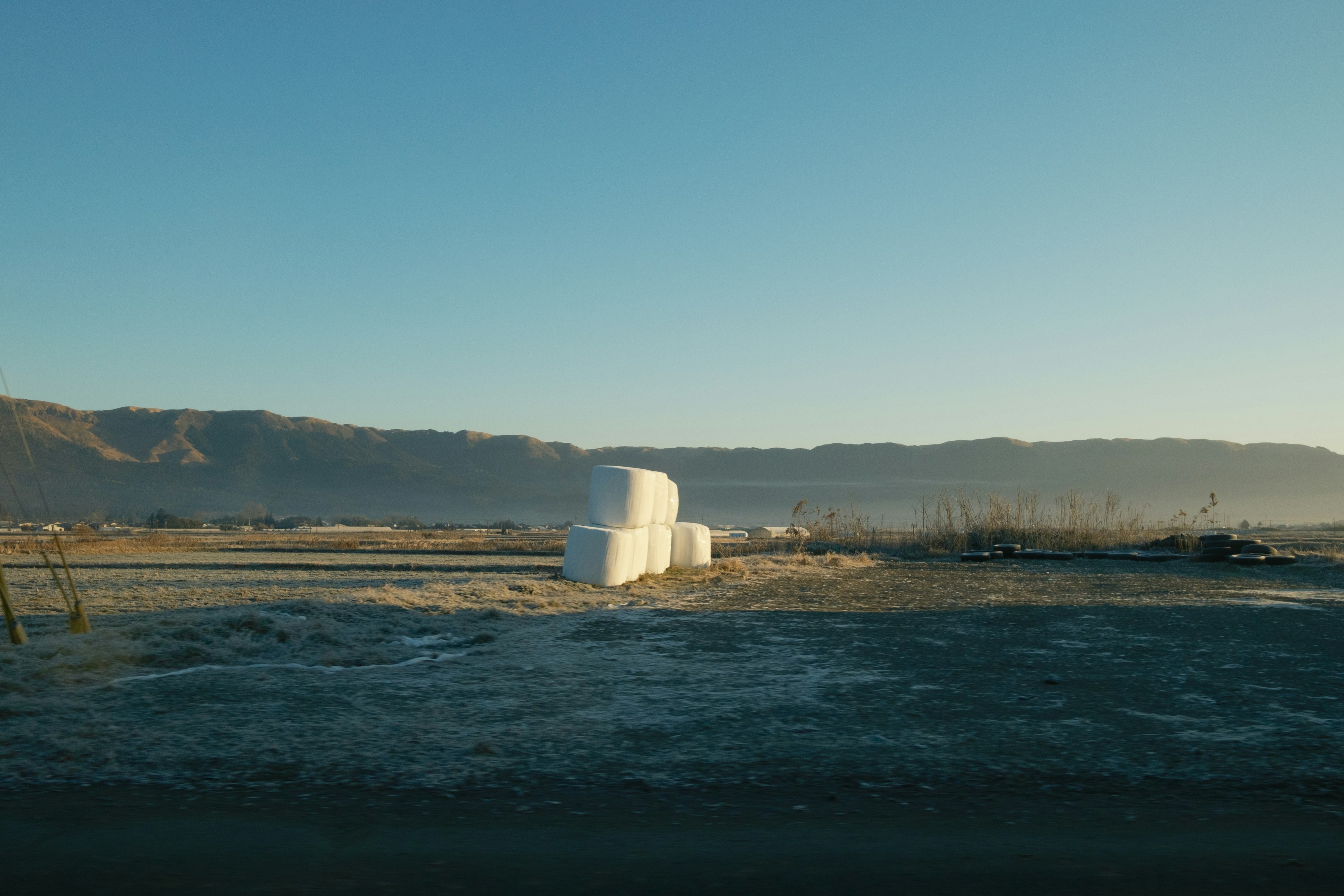 Landscape featuring white hay bales under a blue sky with distant mountains