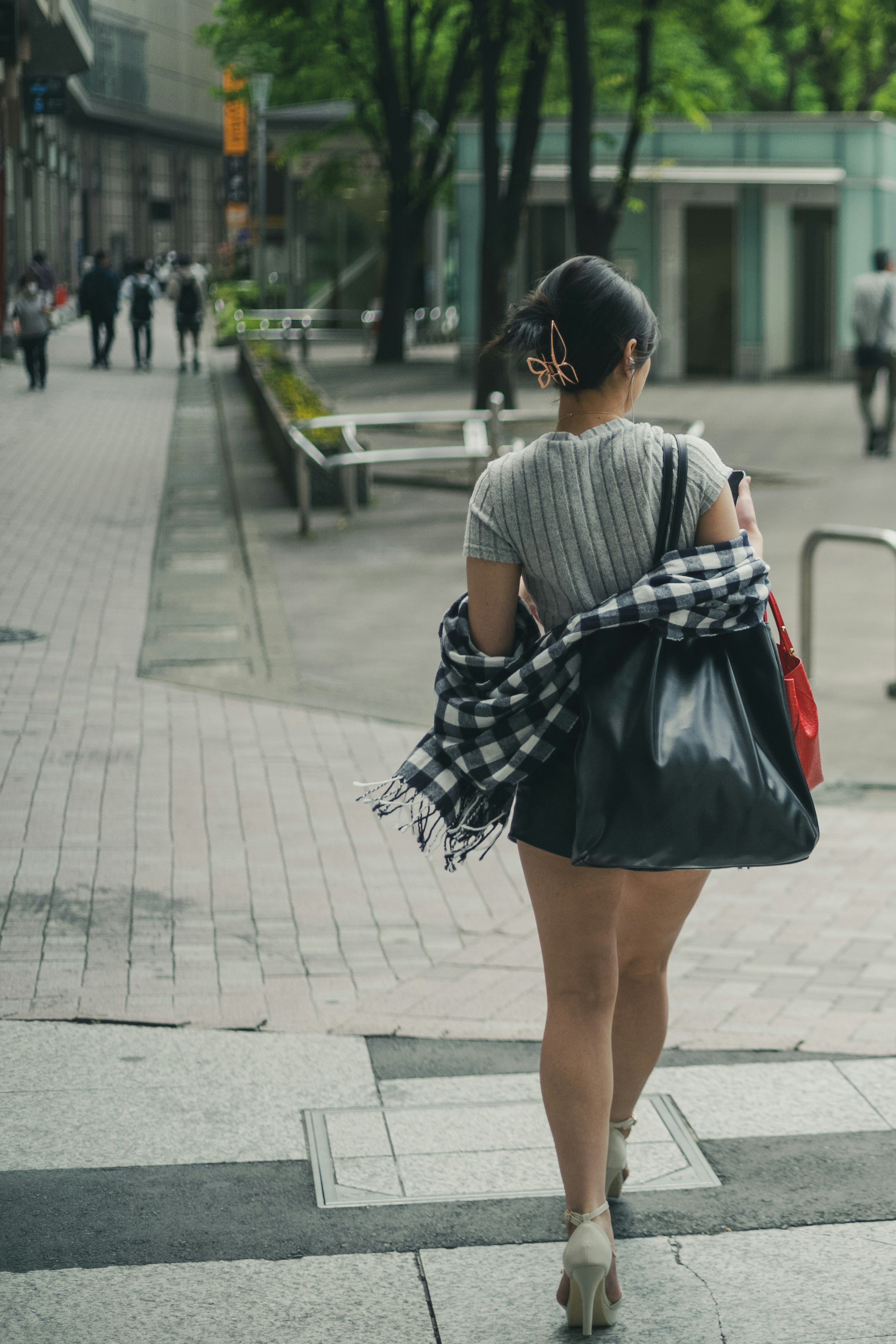 一名女性在城市中走路，肩上背著包，手裡拿著格子襯衫