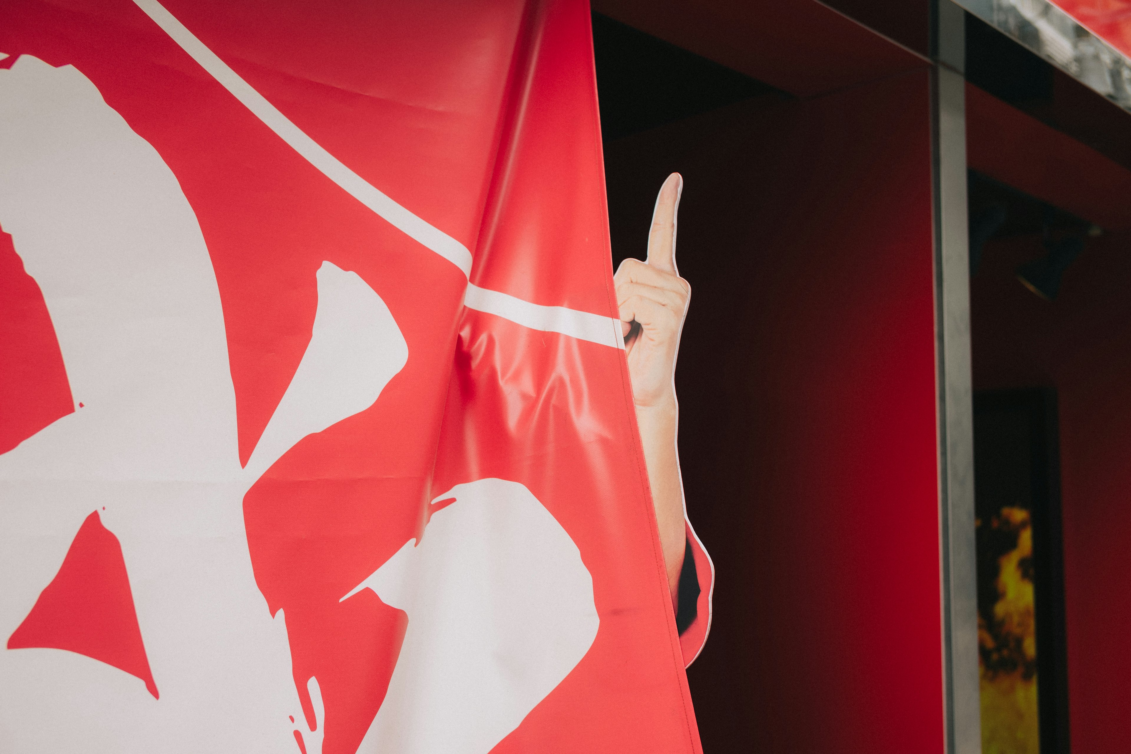 A hand showing the middle finger behind a red flag