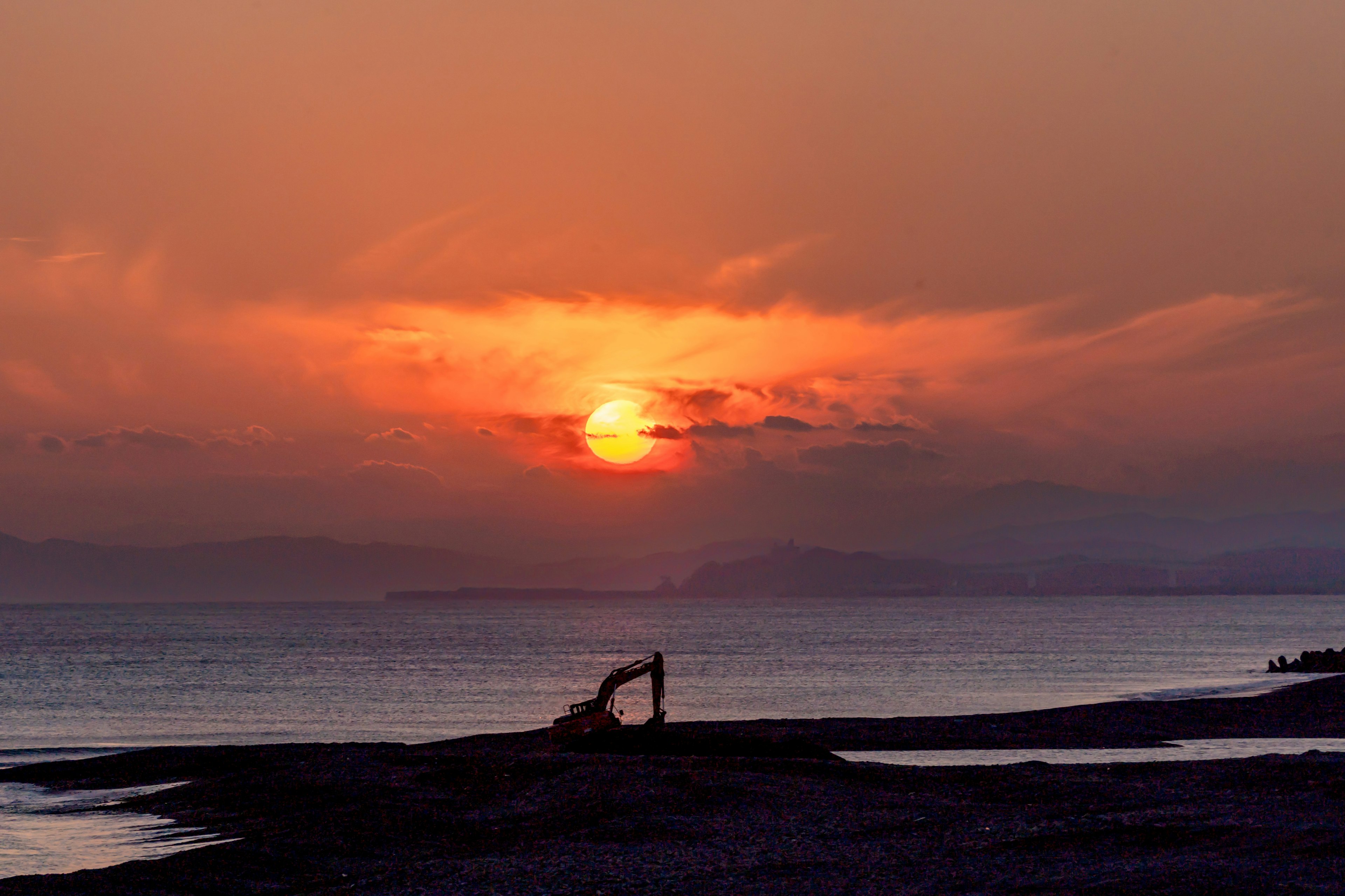 夕日が海に沈む美しい風景 人影と山々が背景に