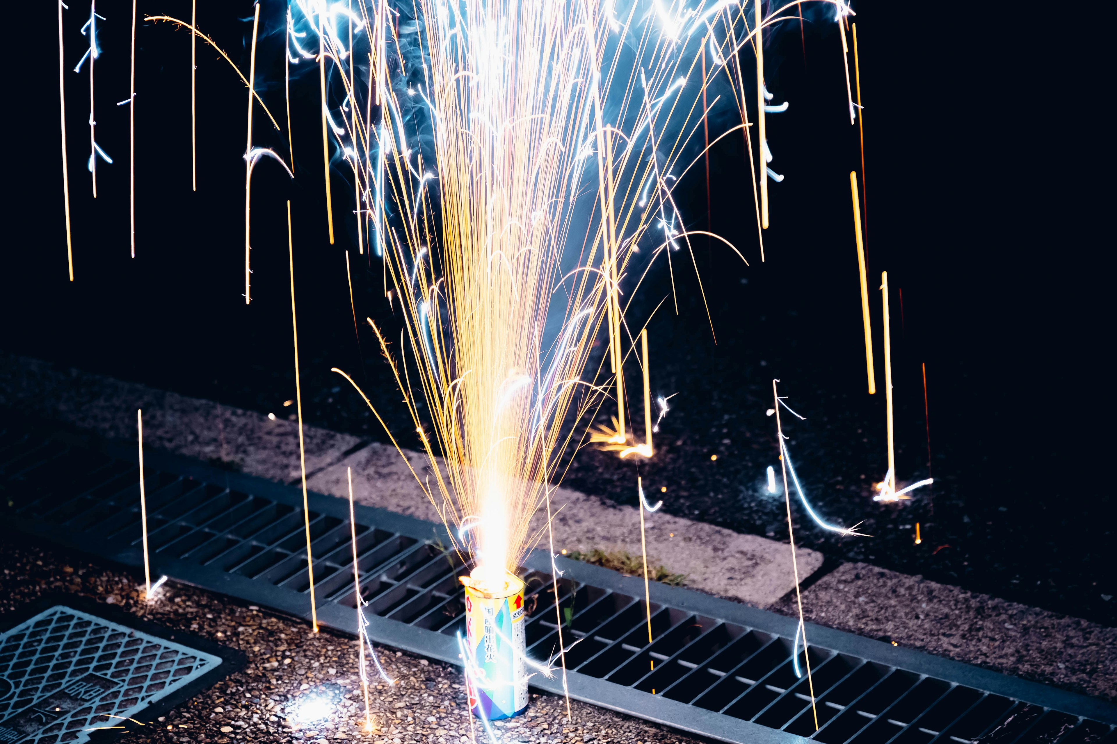 Image capturant des feux d'artifice s'élevant dans le ciel nocturne avec des étincelles dorées et bleues illuminant les environs sombres