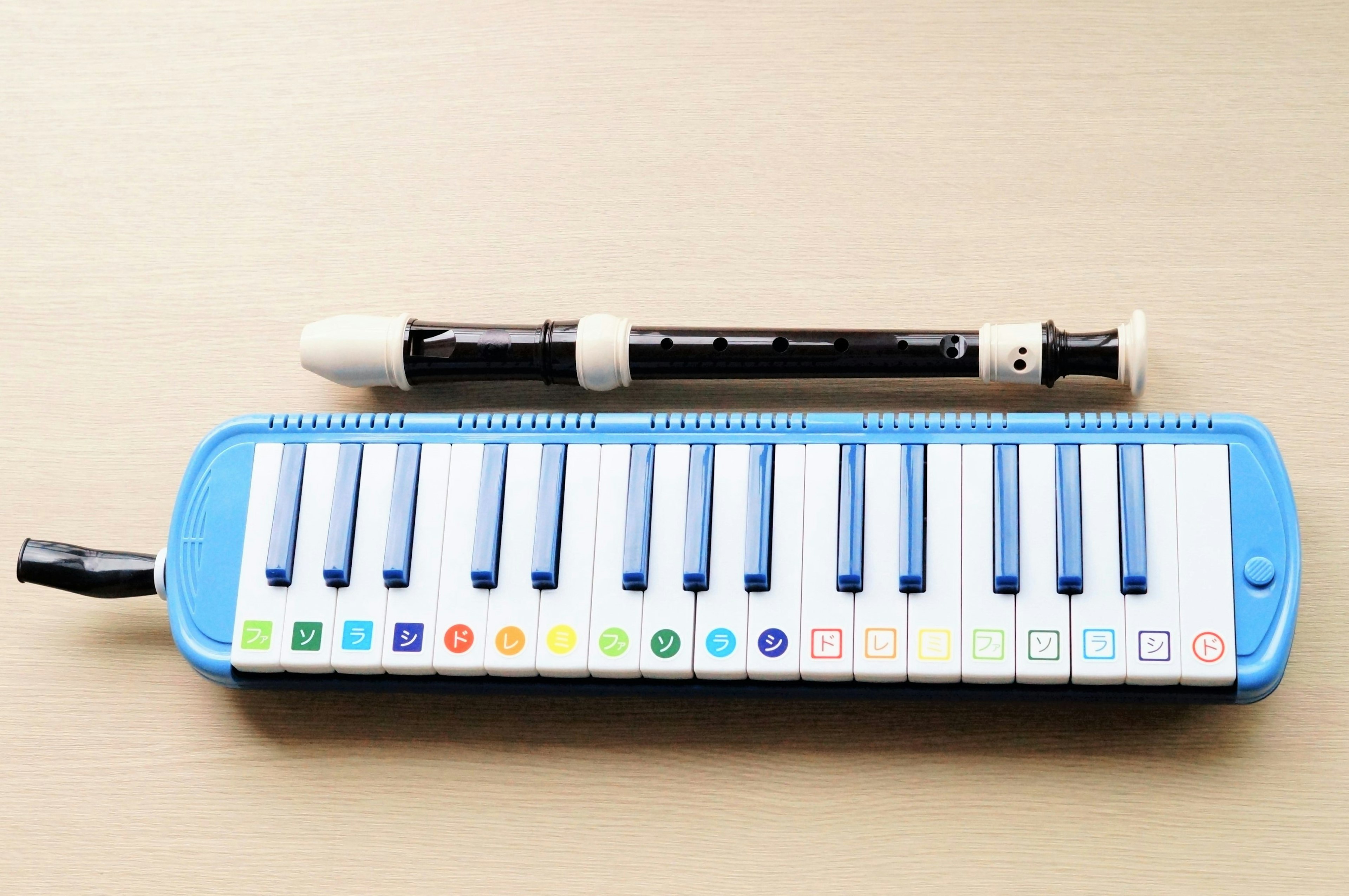 Một cây melodica màu xanh và một cây recorder màu đen đặt trên bàn gỗ