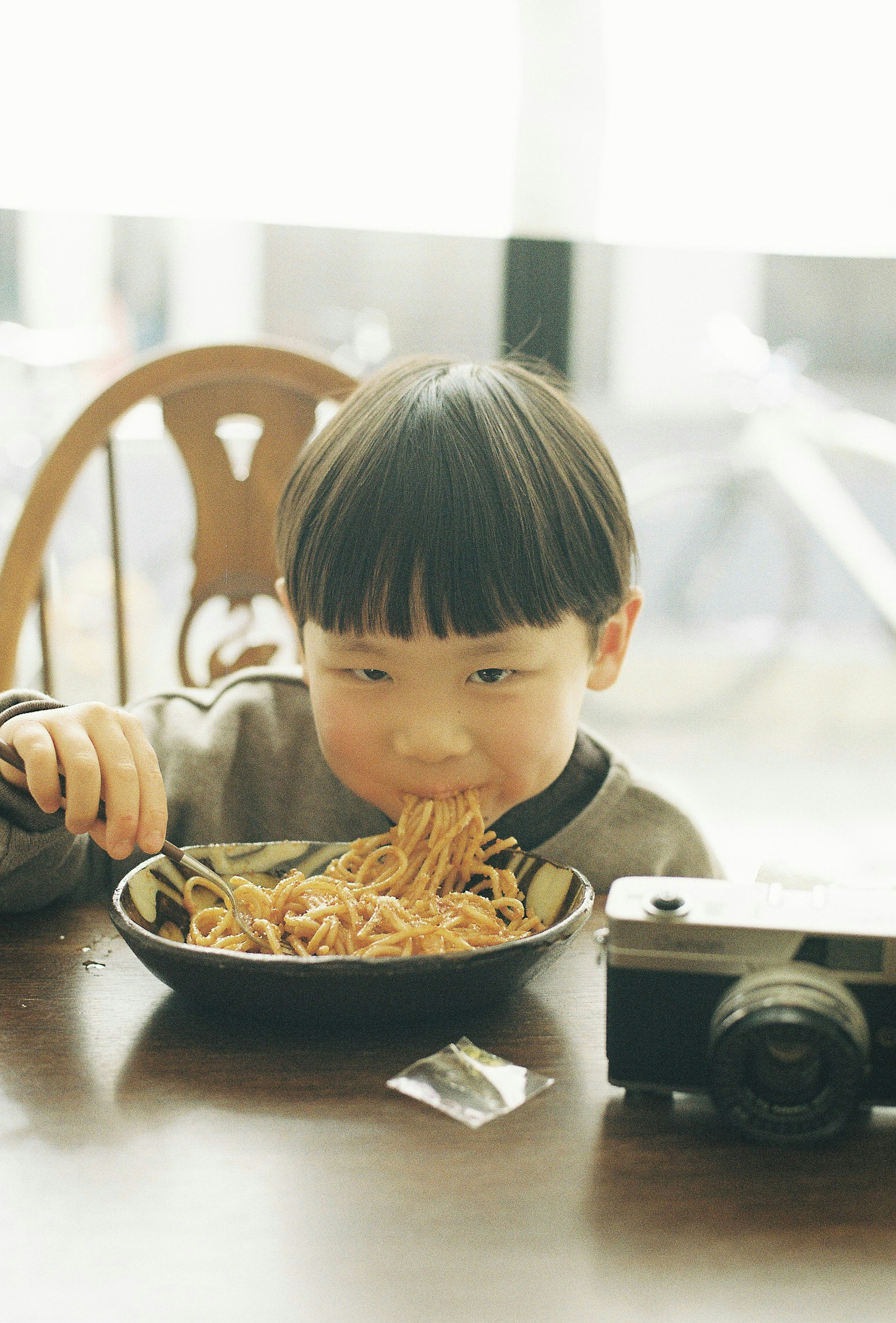 Niño comiendo fideos al lado de una cámara