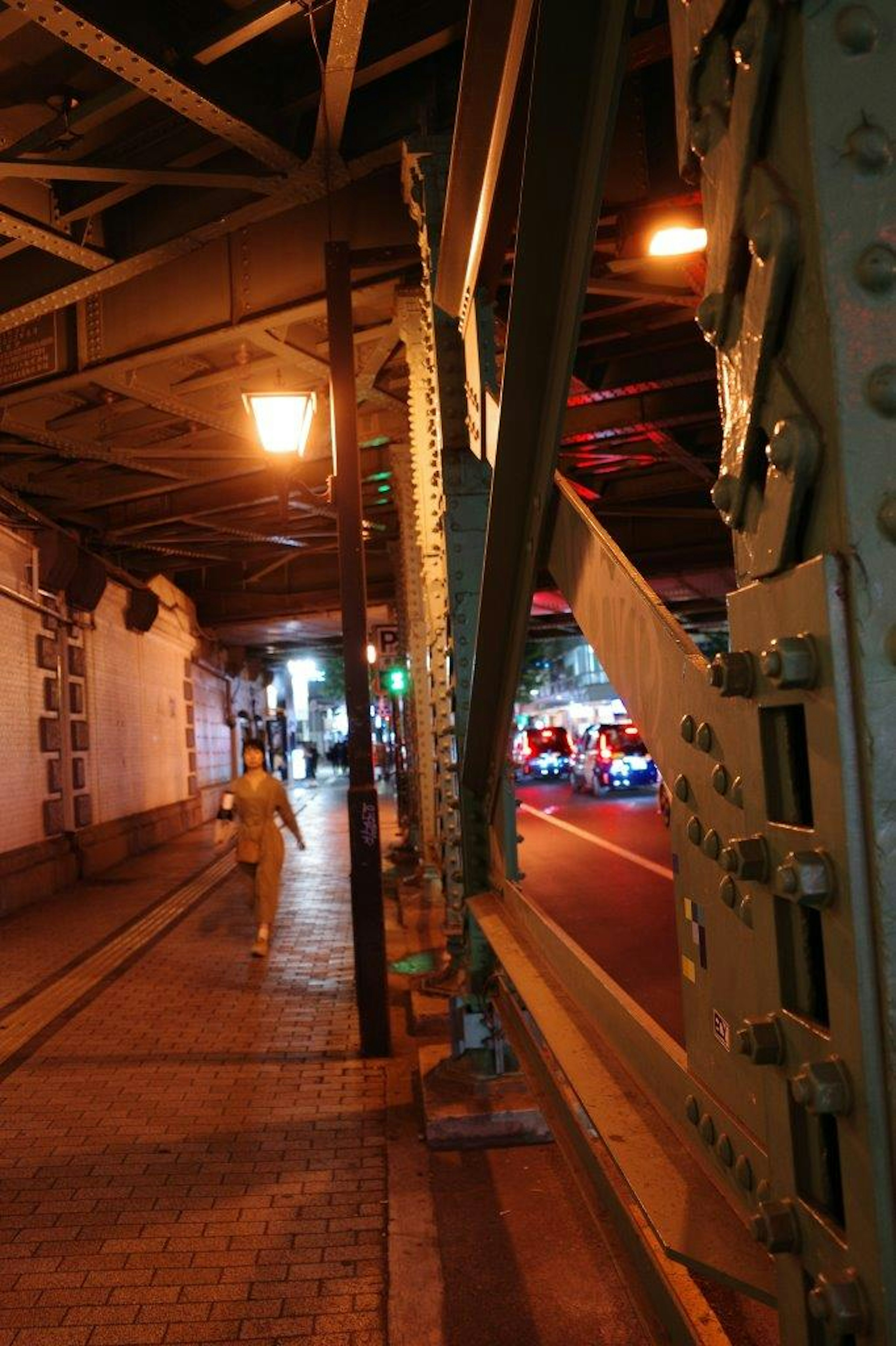 Nighttime urban scene featuring a person walking under a bridge with streetlights and passing cars