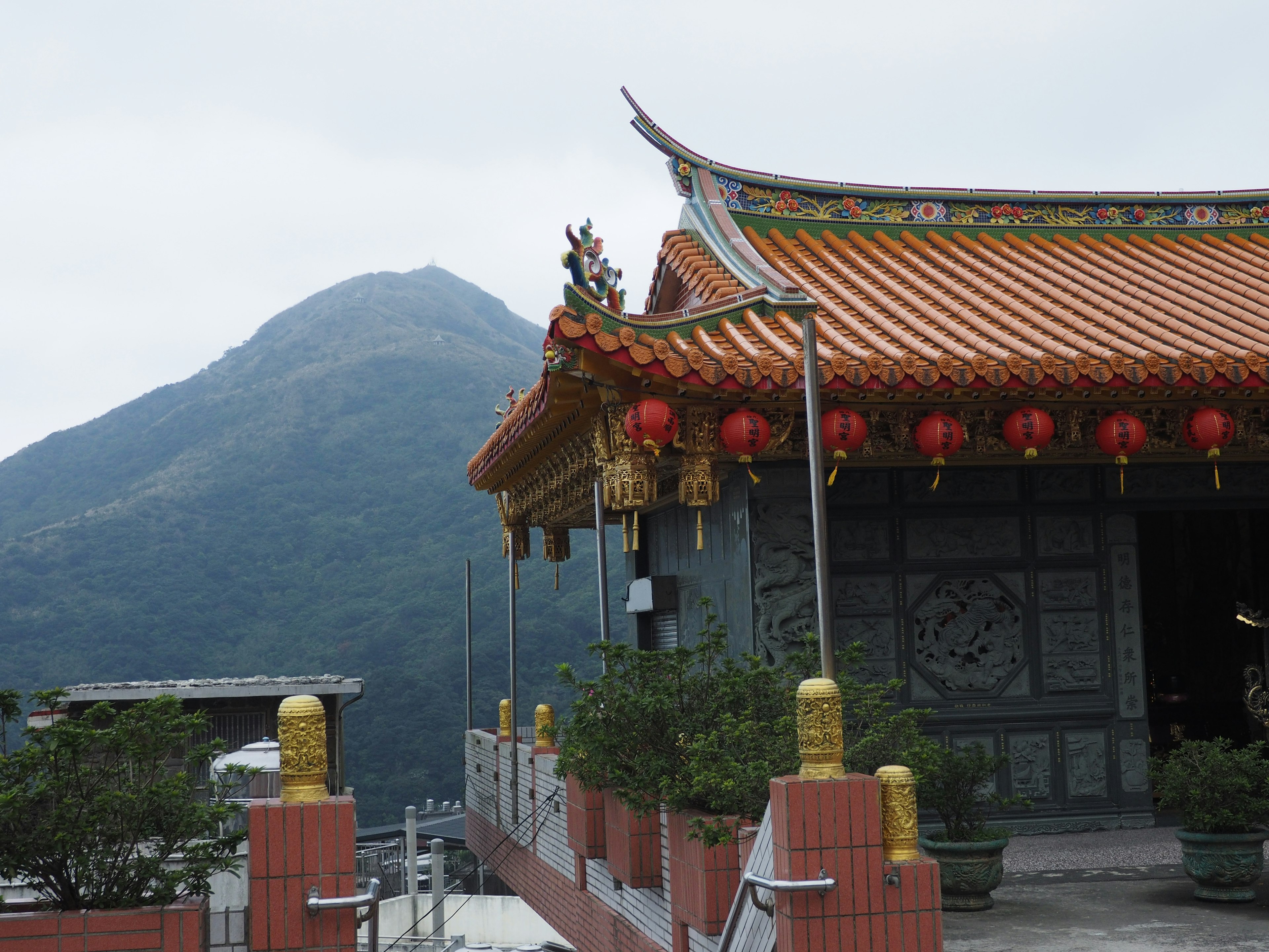 Vue pittoresque d'un temple avec un toit orné et des lanternes rouges devant un paysage montagneux