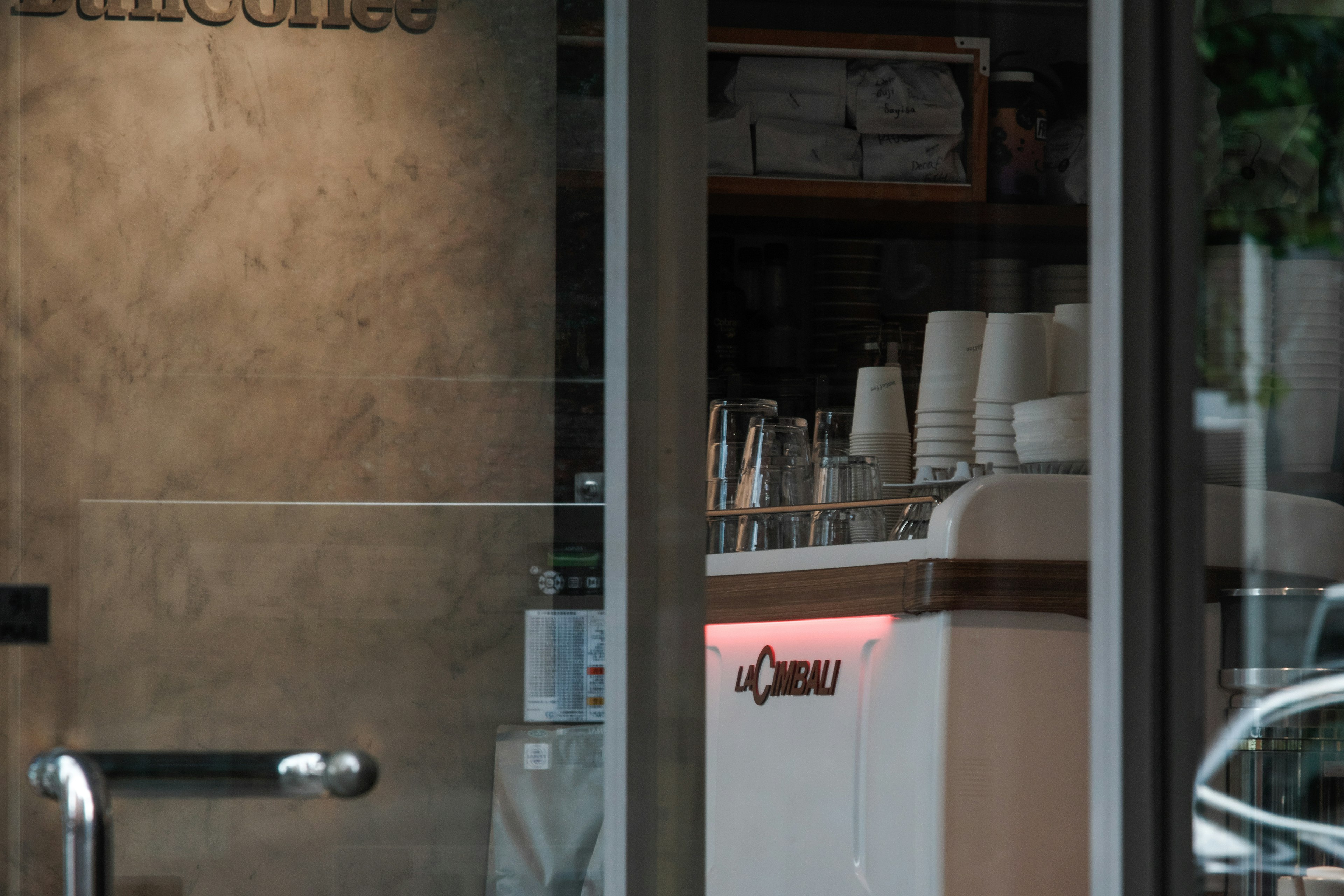 Imagen de un interior de café visible a través de una ventana con una máquina de café blanca y tazas ordenadas