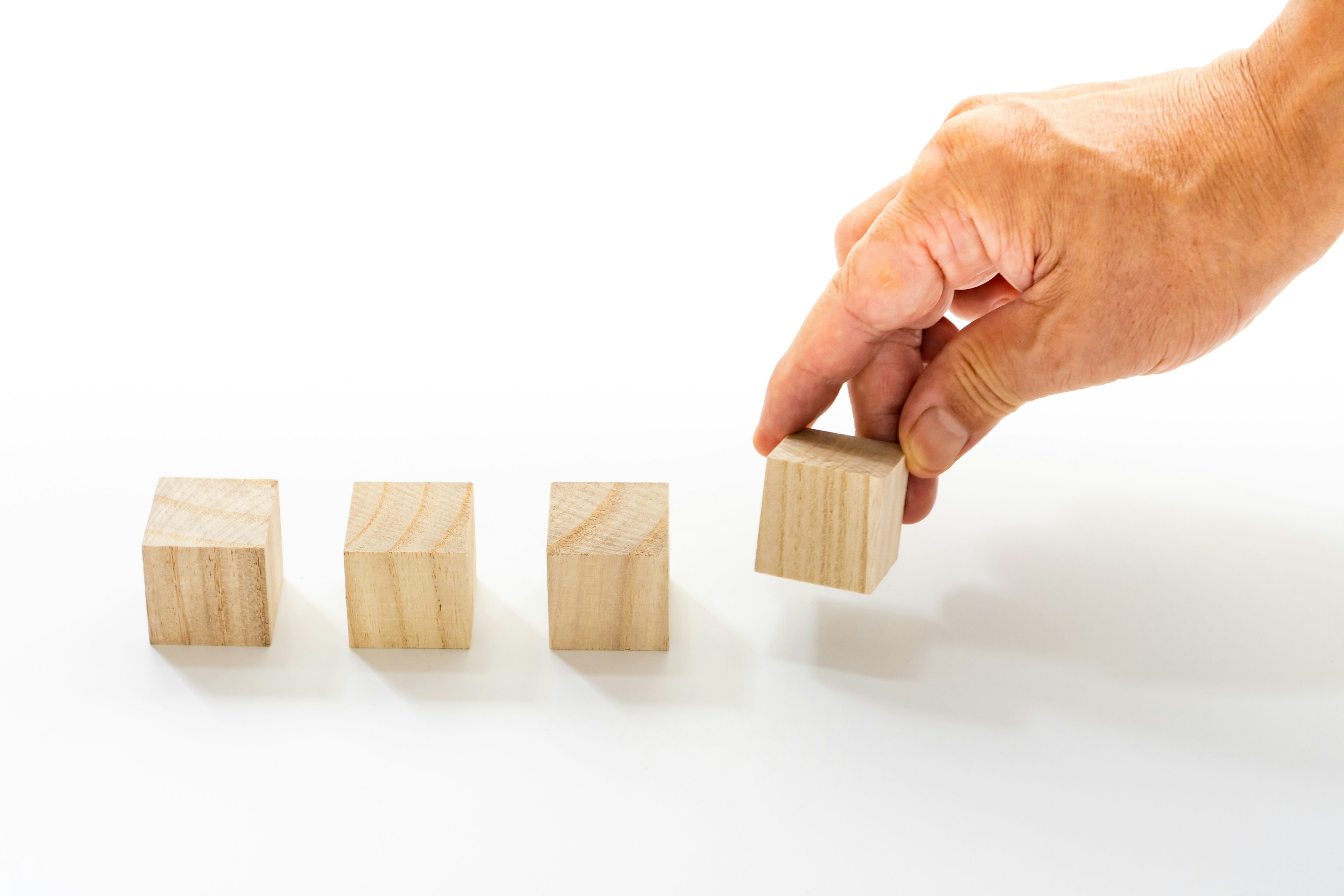 A hand lifting a wooden block from a row of three blocks