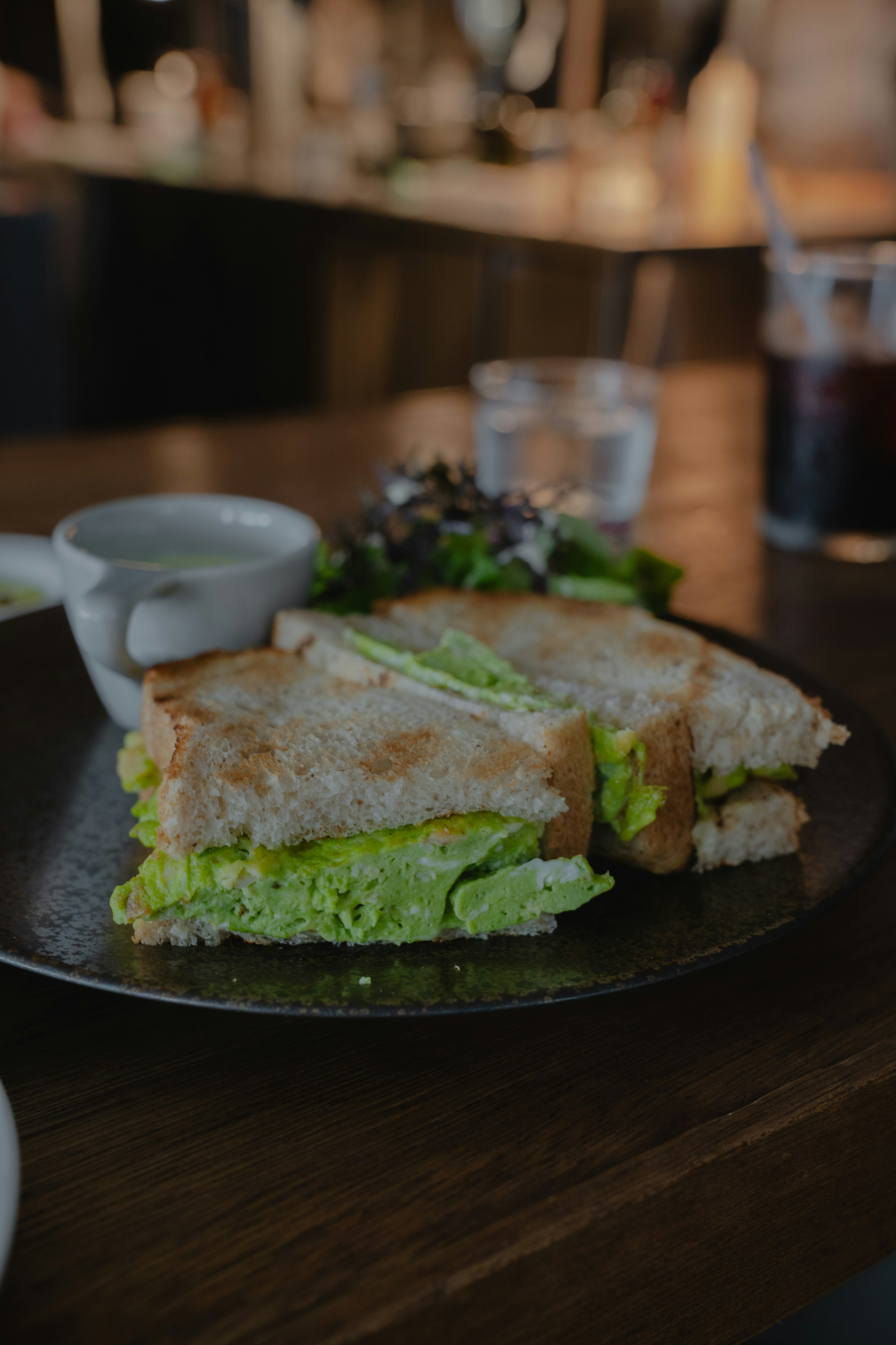 Un panino con lattuga verde su un piatto accompagnato da una piccola salsa e insalata