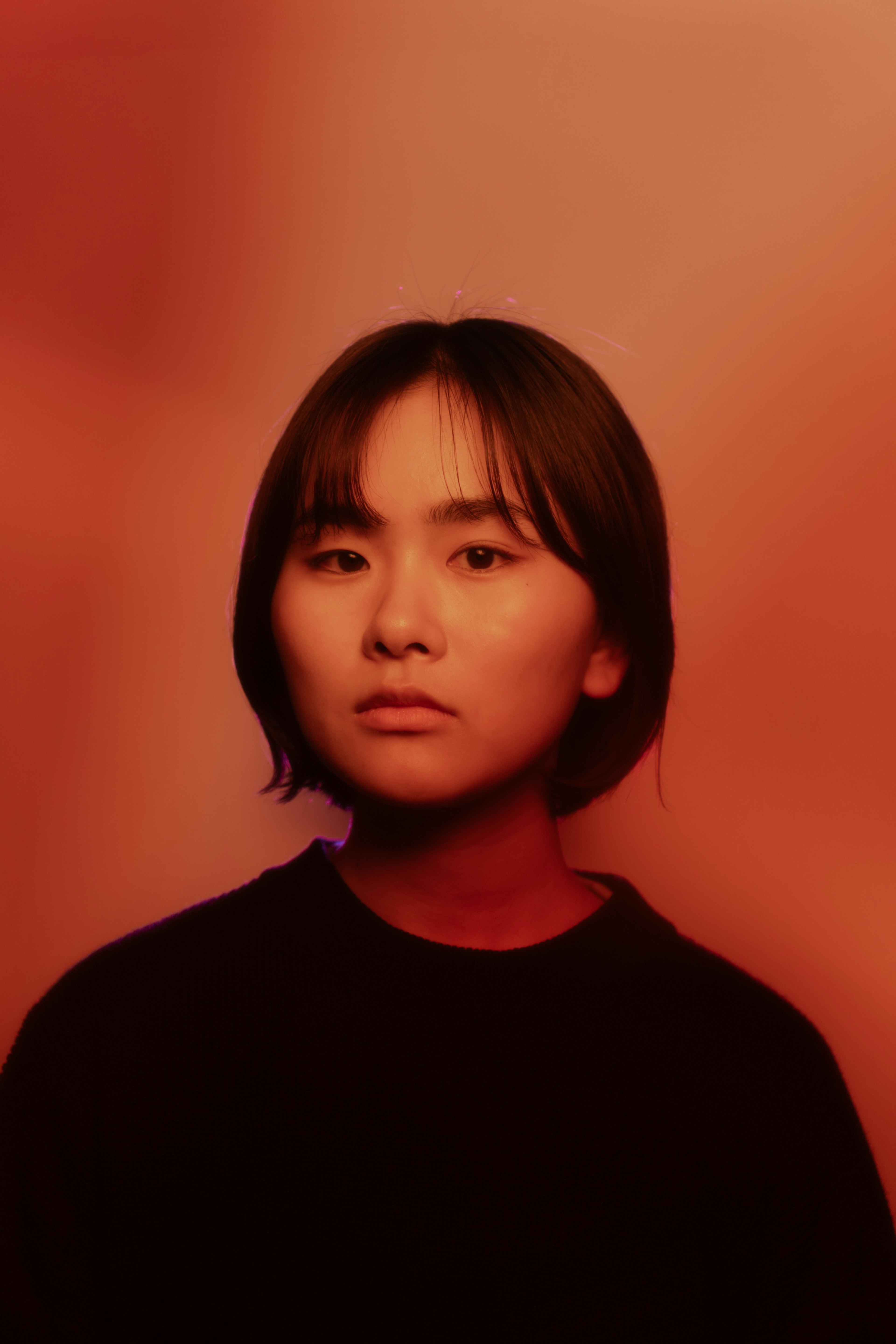 Portrait of a young woman with a serious expression against a red background