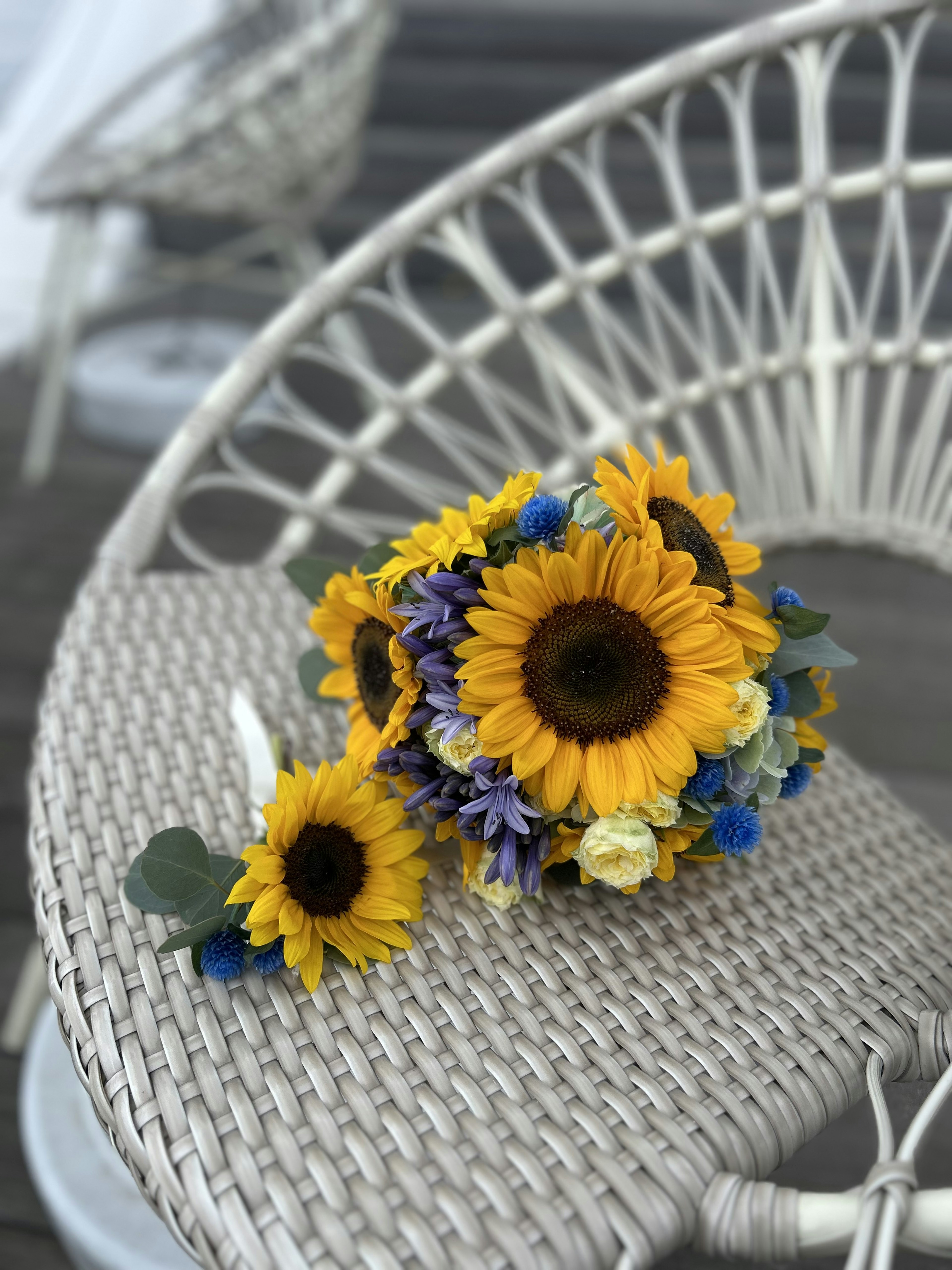 Ein schöner Strauß aus Sonnenblumen und blauen Blumen auf einem weißen Stuhl