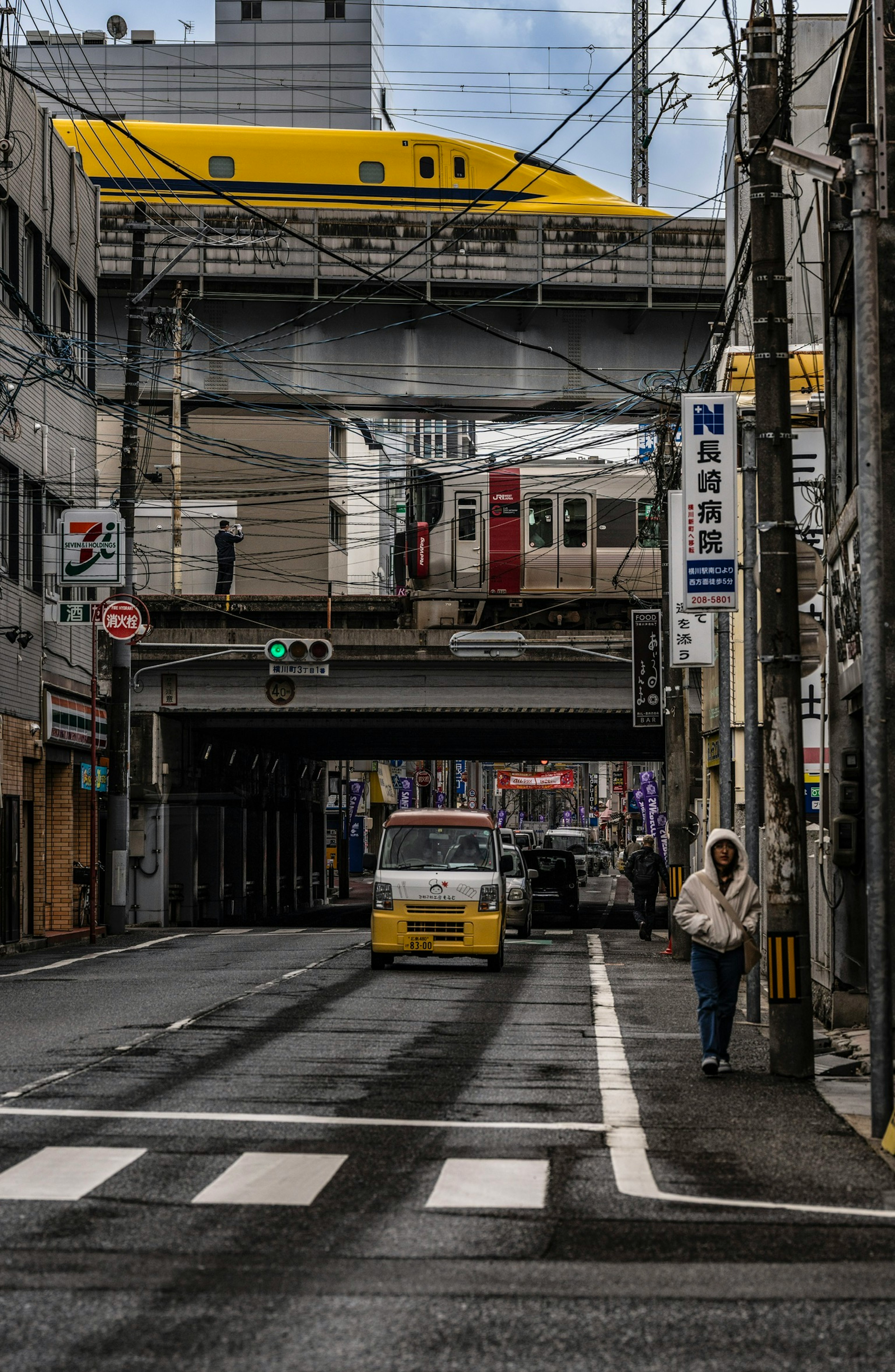 Urban scene featuring a yellow train above a street with a pedestrian