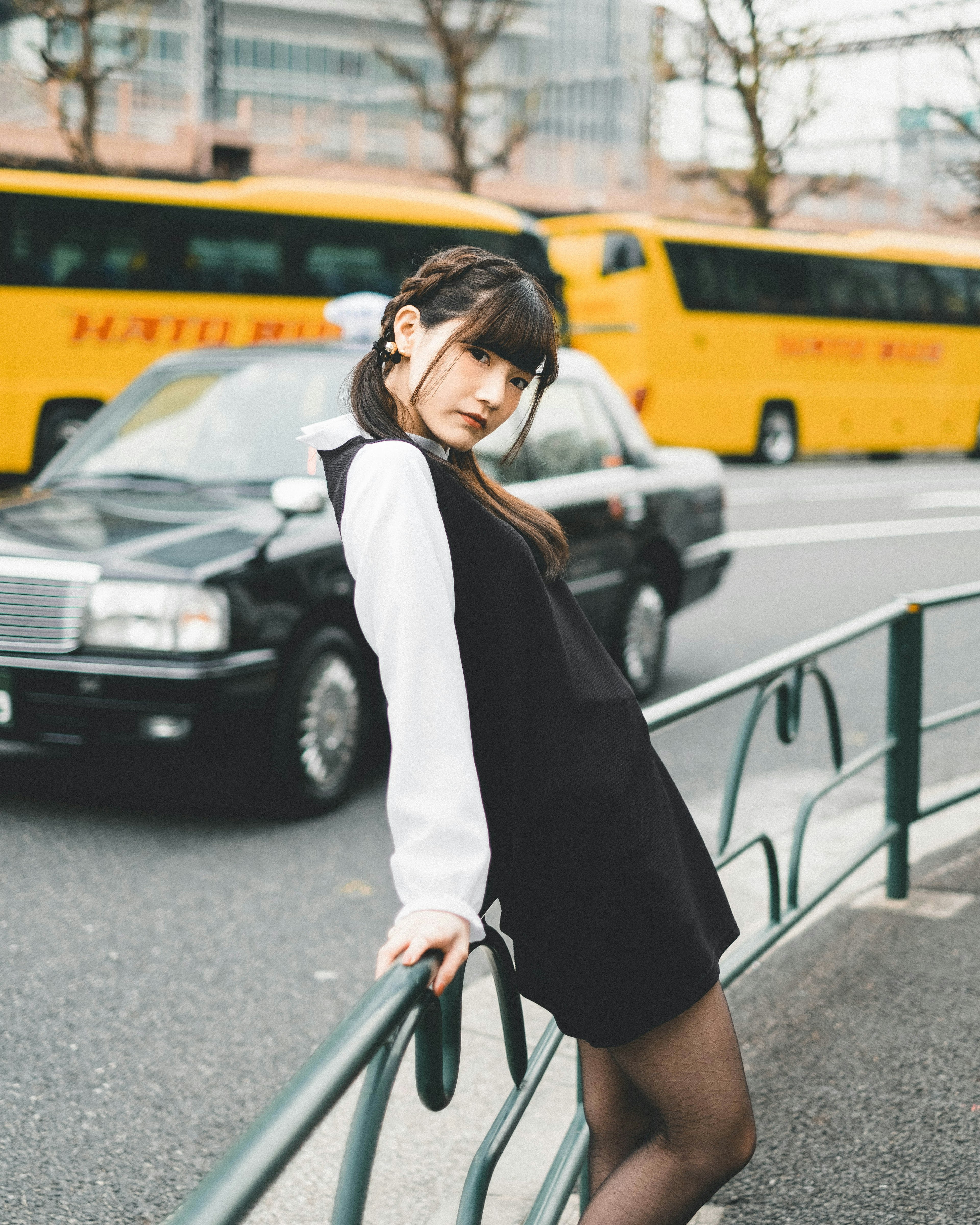 Foto de moda de una mujer posando en la calle vestida de negro y blanco autobús amarillo y coche negro de fondo