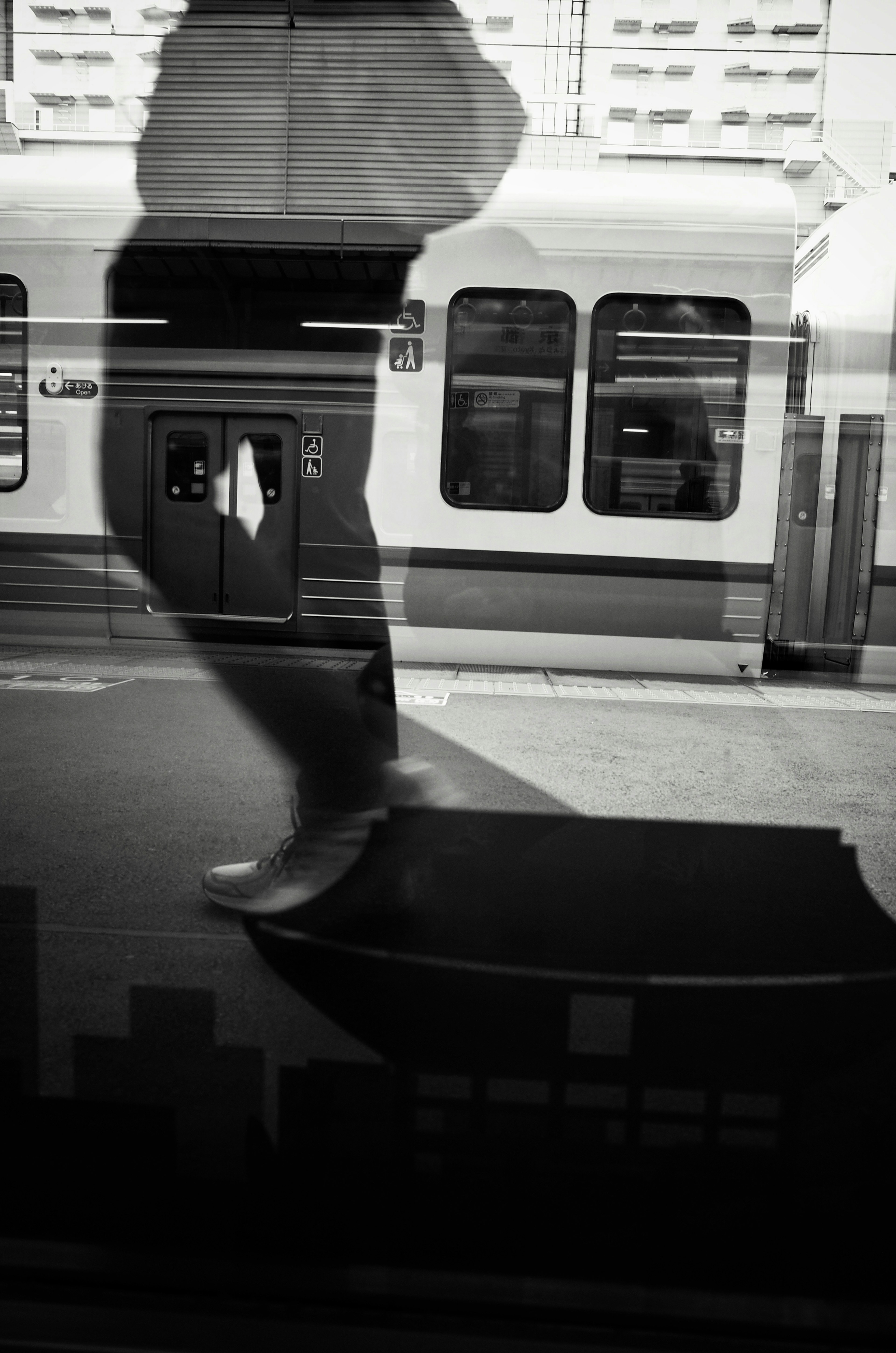 Una sombra de una persona caminando reflejada en una ventana de tren en blanco y negro