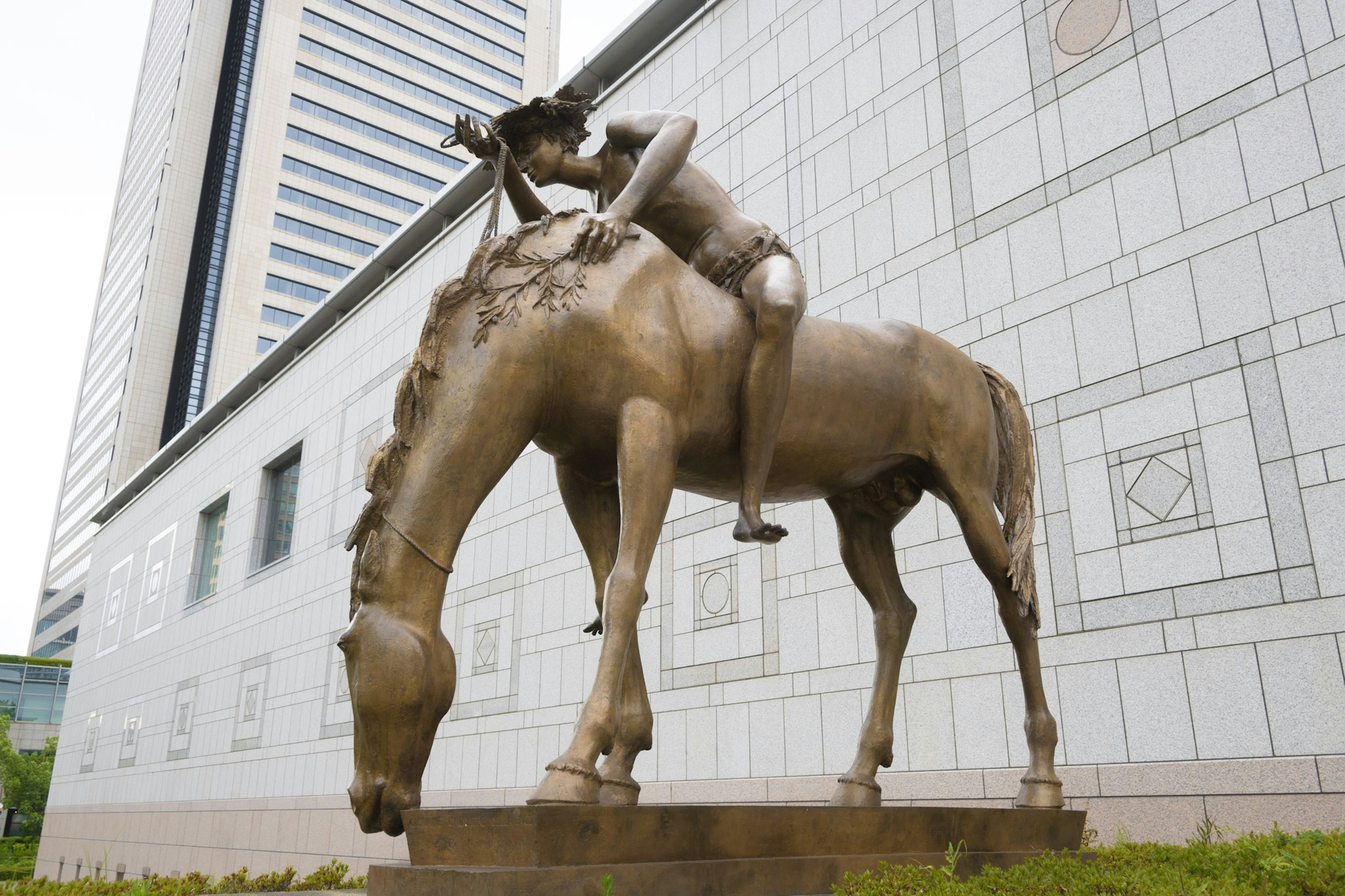 Escultura de bronce de una persona montando un caballo frente a un edificio