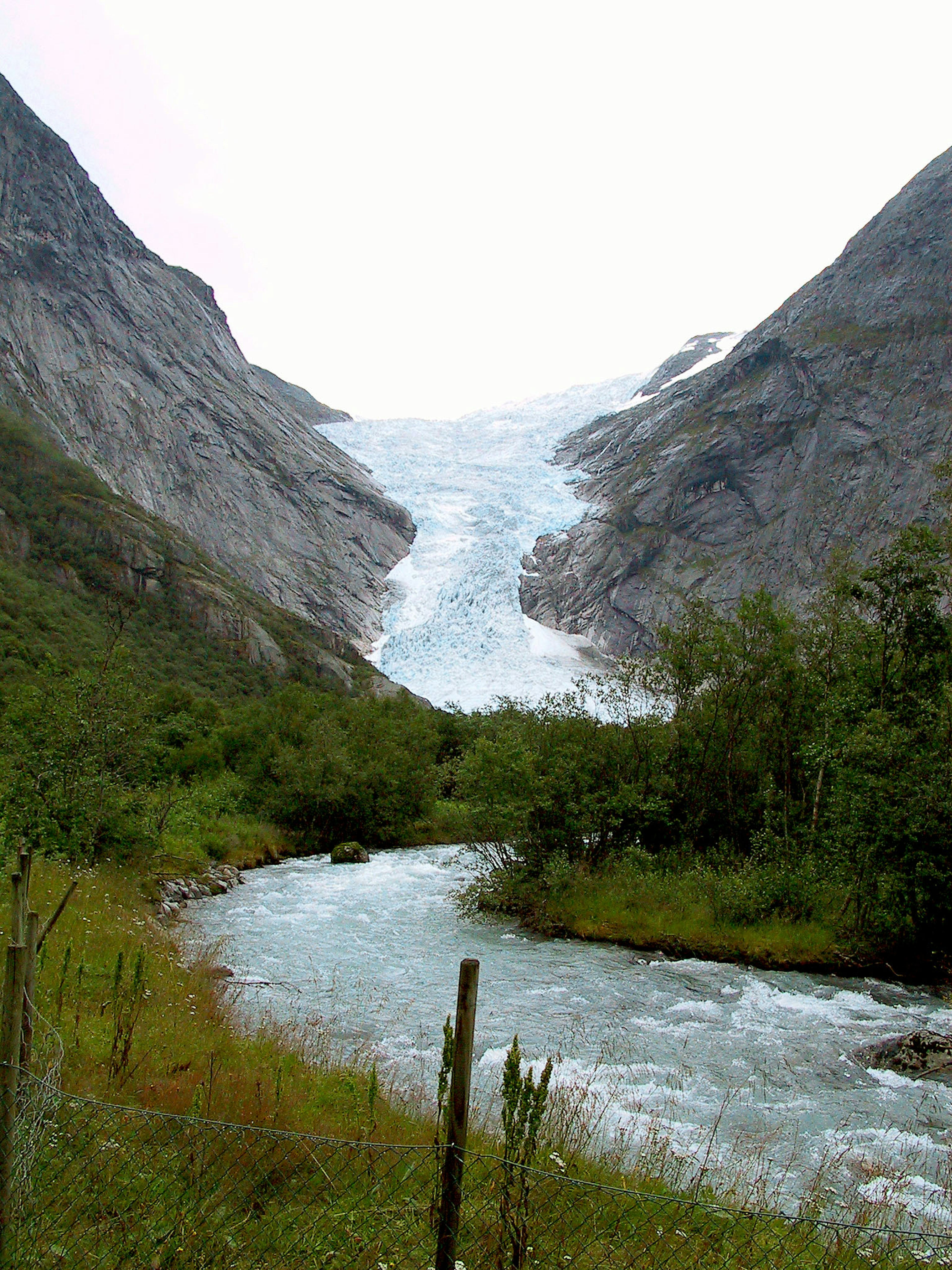 Paysage montagneux avec un glacier descendant une vallée entourée d'herbe verte et d'une rivière