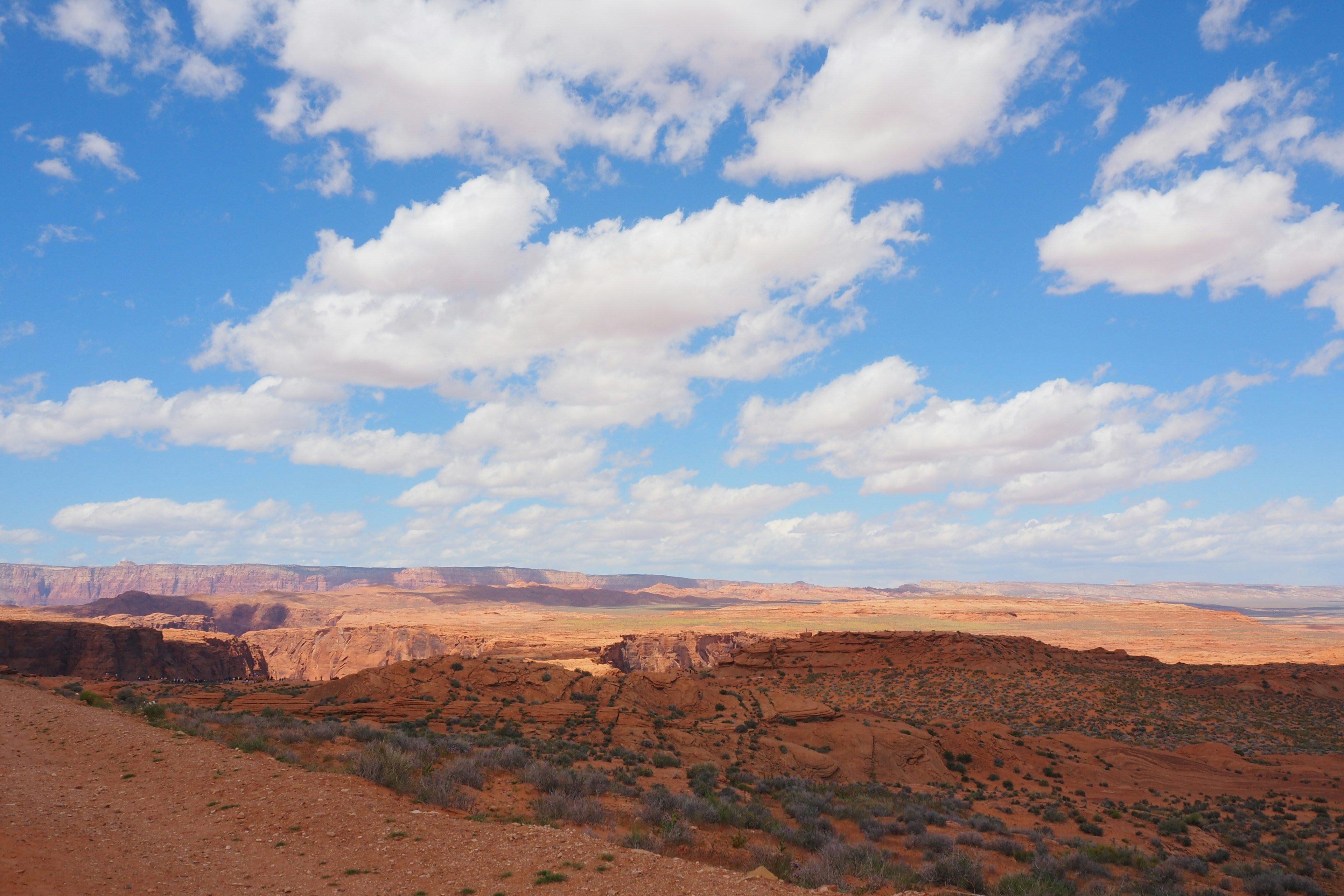 Amplio paisaje con formaciones rocosas rojas y un cielo azul brillante con nubes