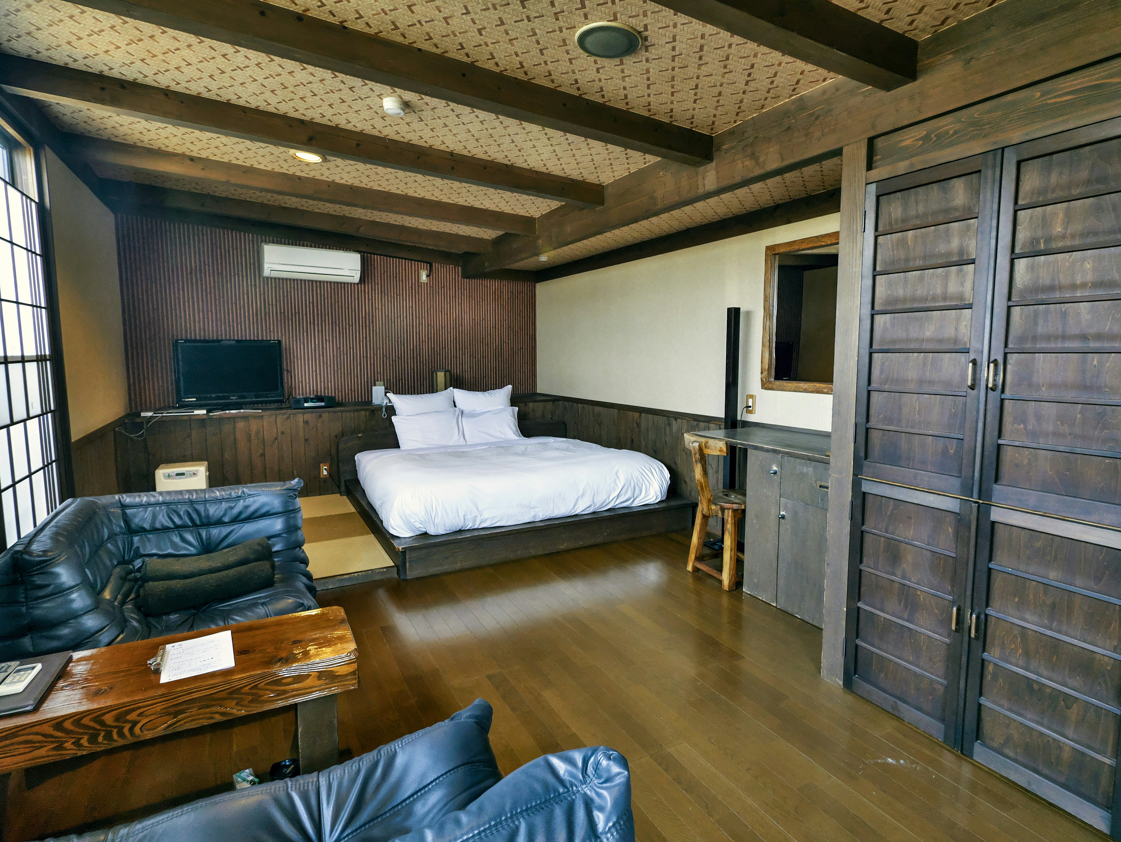 Simple modern Japanese-style bedroom with wooden beams and flooring large bed and sofa TV and air conditioning