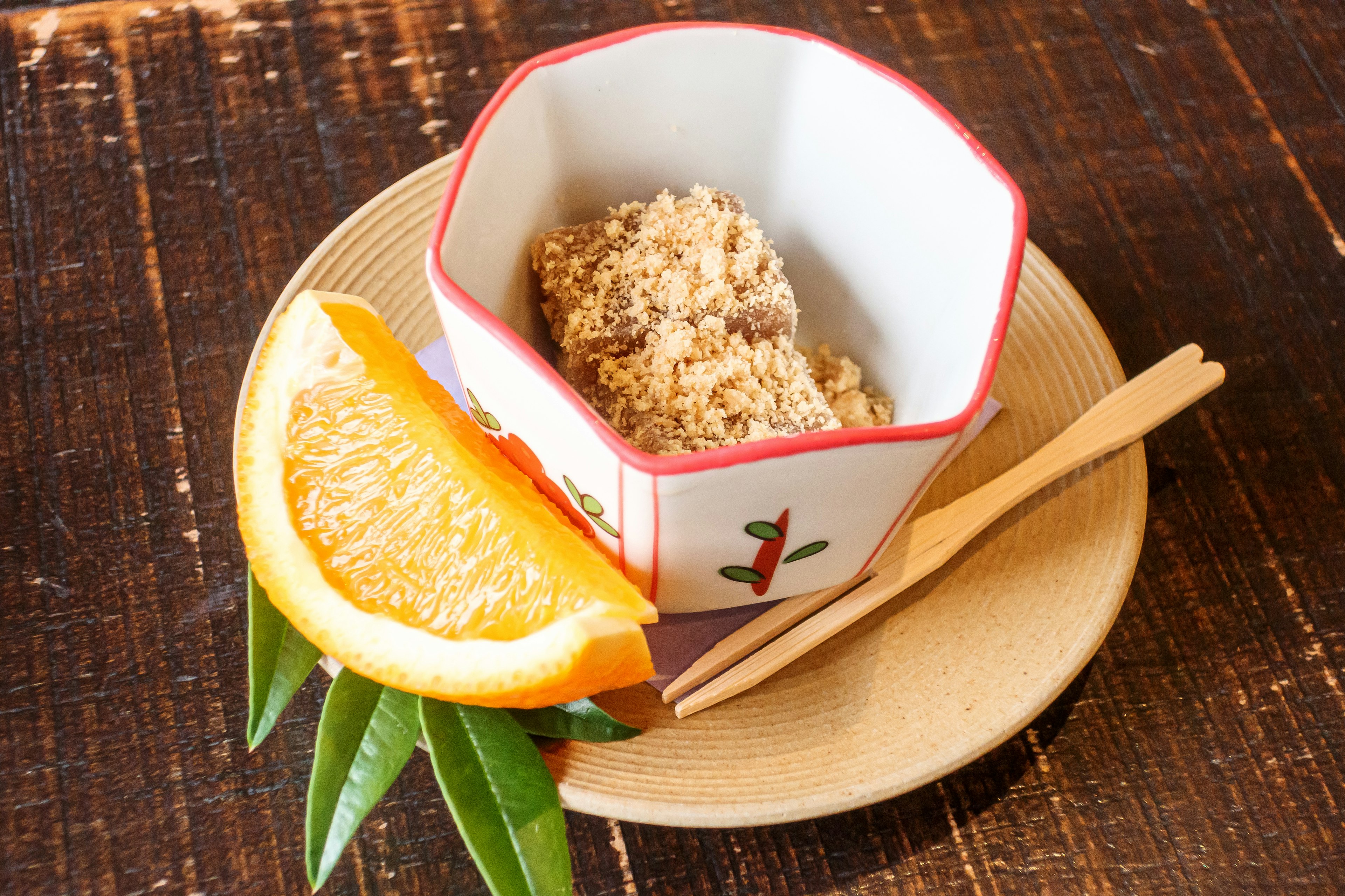 Plato elegante de postre japonés servido en un tazón octagonal con una rodaja de naranja y hojas