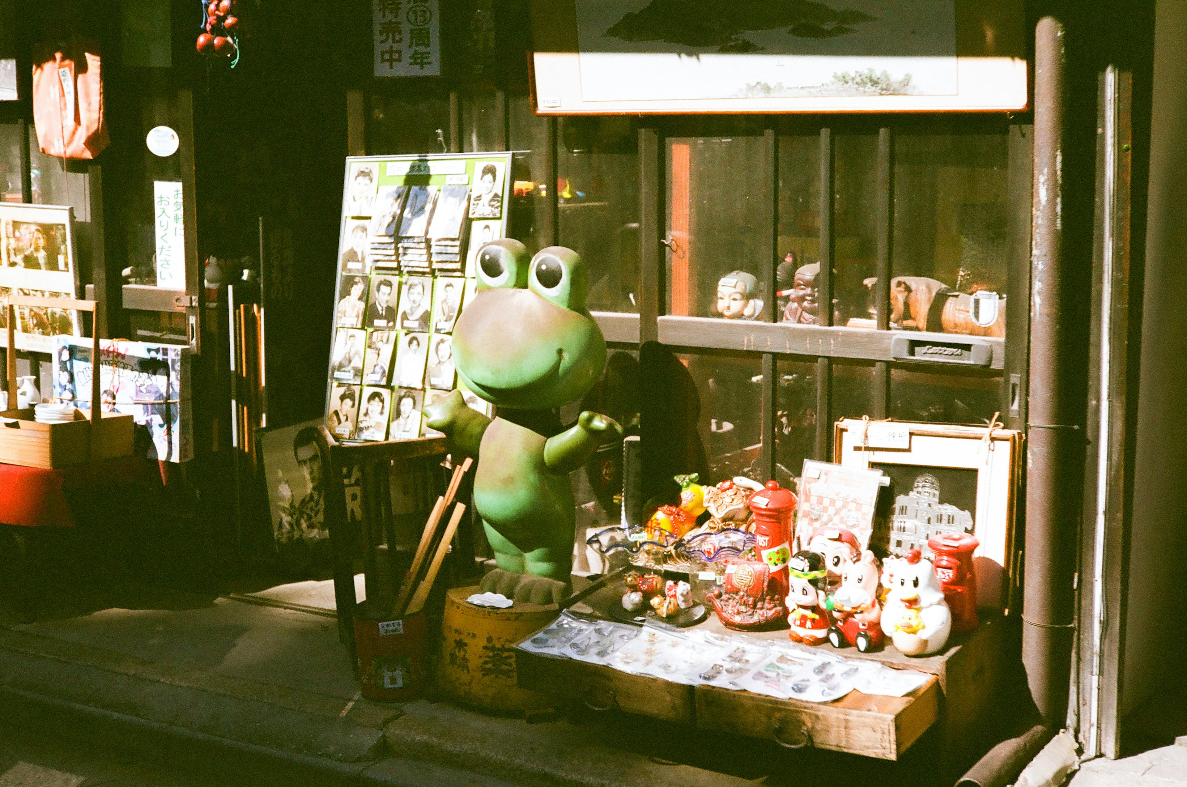 绿色青蛙吉祥物站在商店前面，周围有各种糖果和纪念品