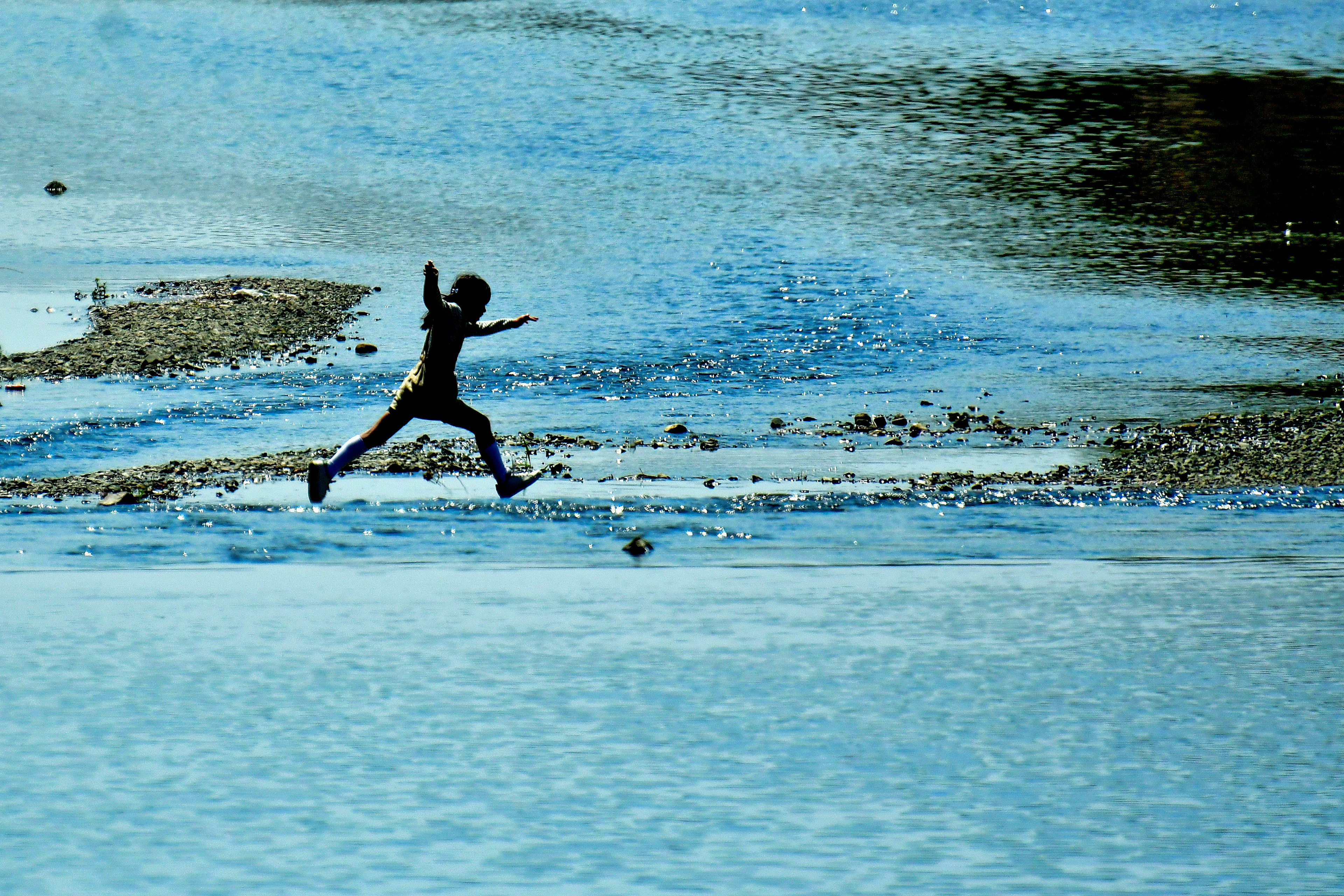 Silhouette of a child running on a blue water surface