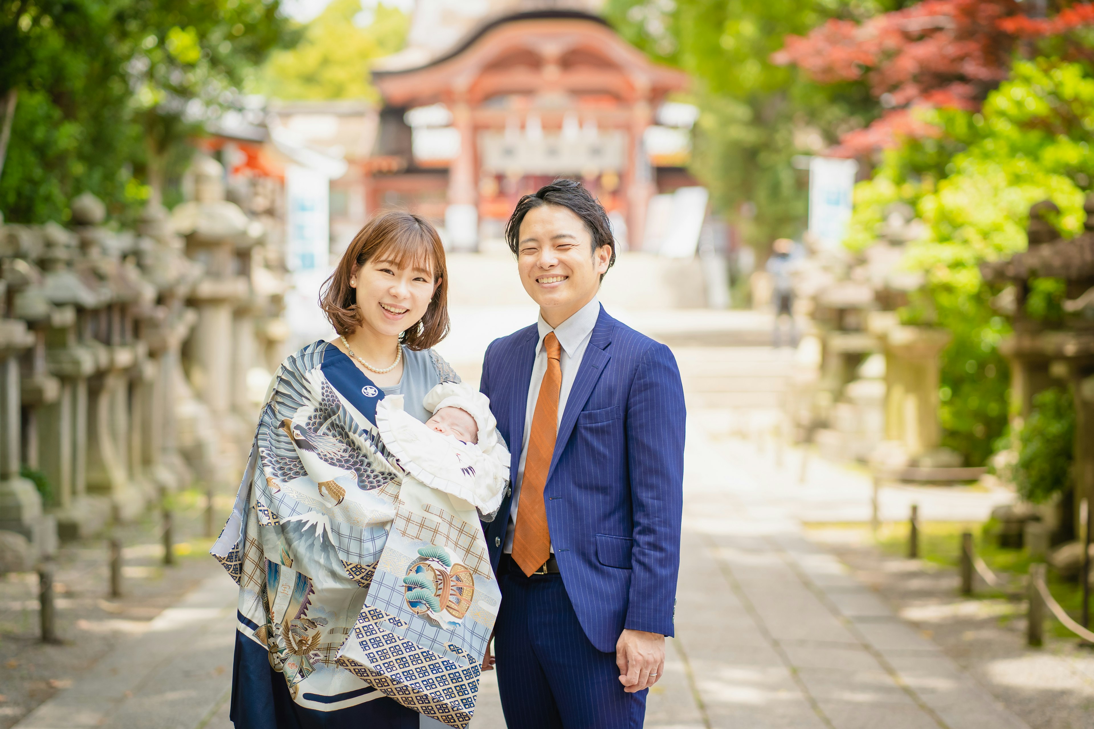 家族が神社の前で写真を撮っている赤ちゃんを抱いた母親と父親