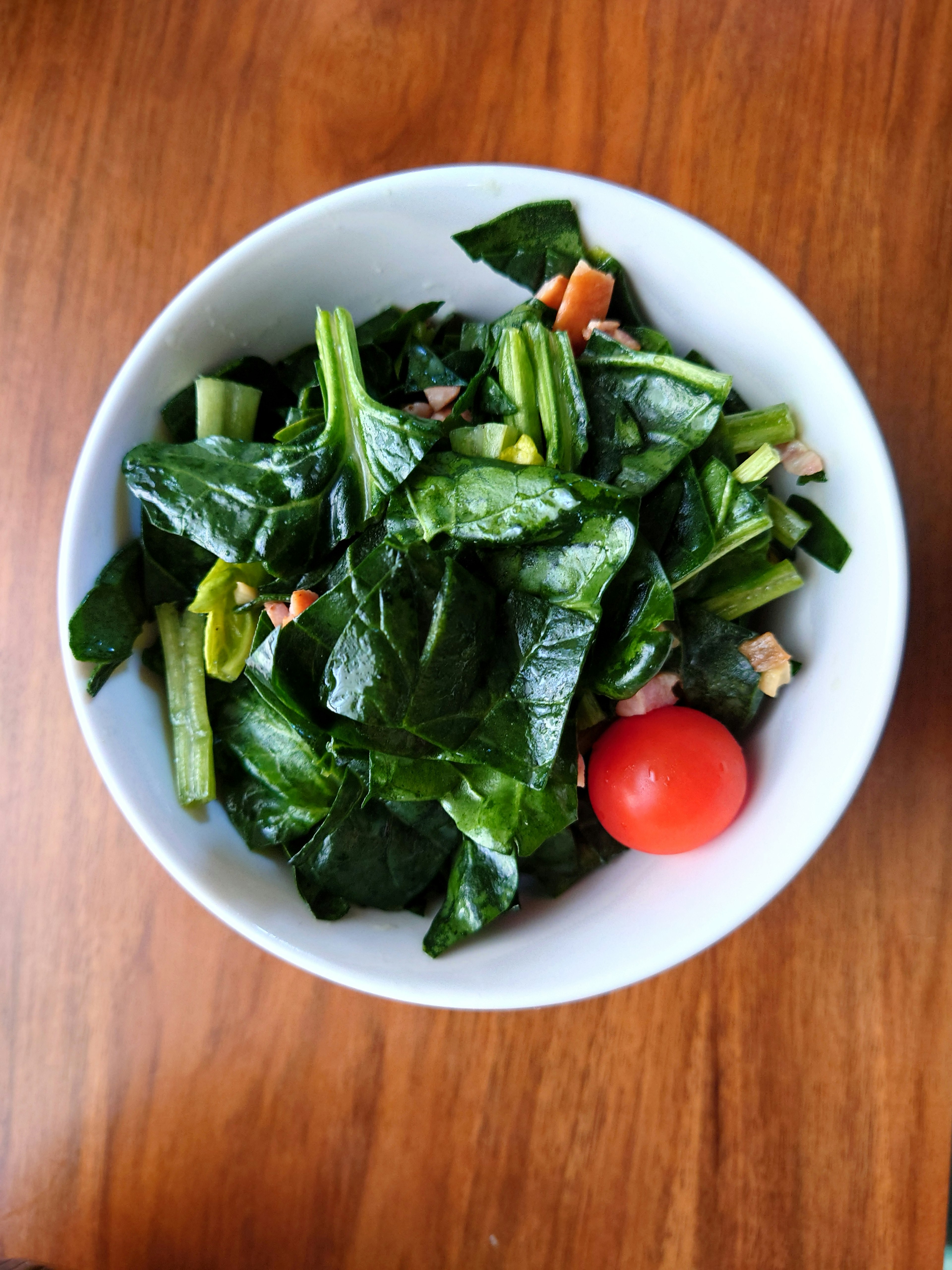 Salad bayam segar dalam mangkuk dengan satu tomat