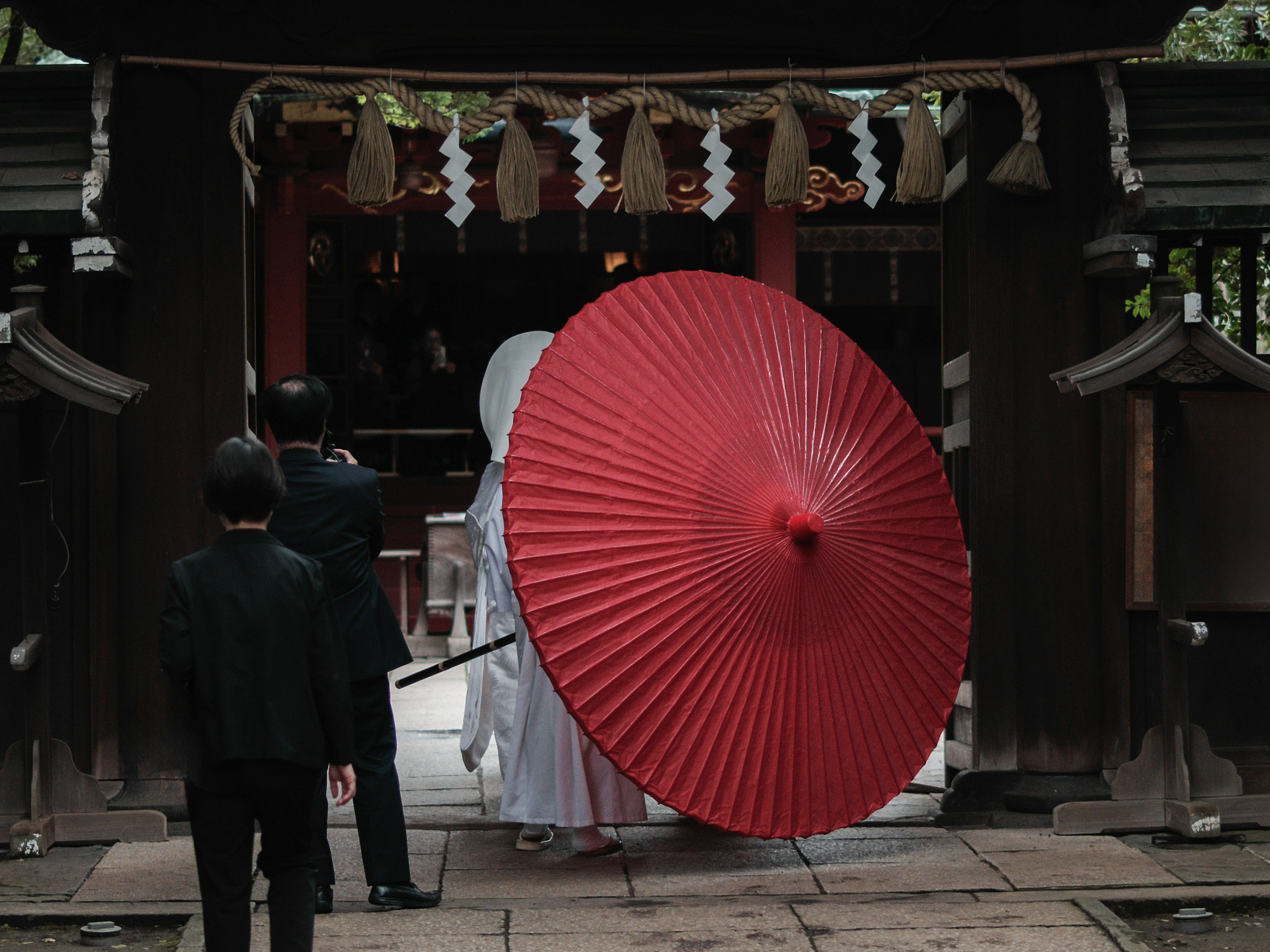 Mariée en tenue traditionnelle tenant un parapluie rouge entrant dans un sanctuaire