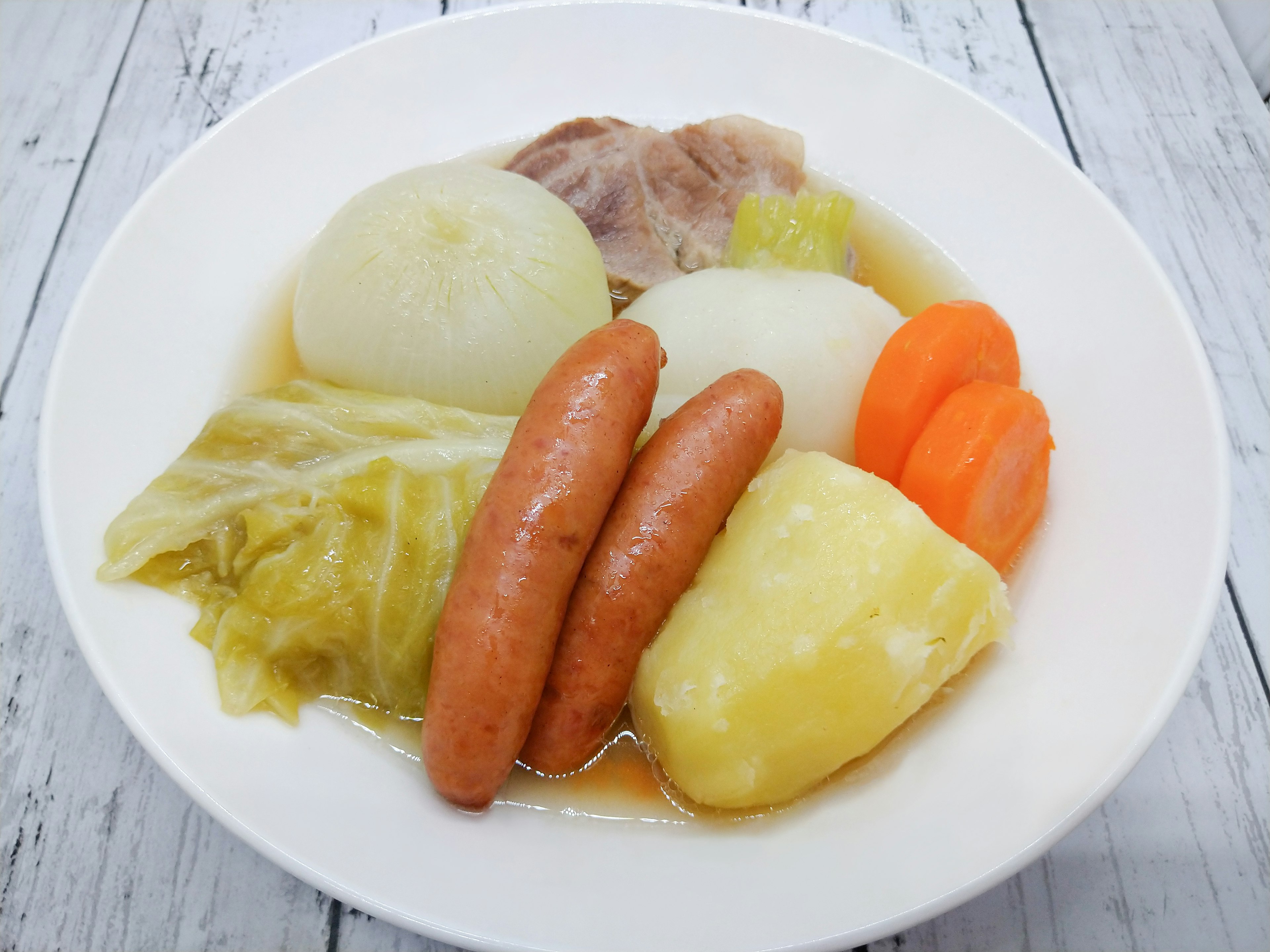 A stew with vegetables and sausages served in a white bowl