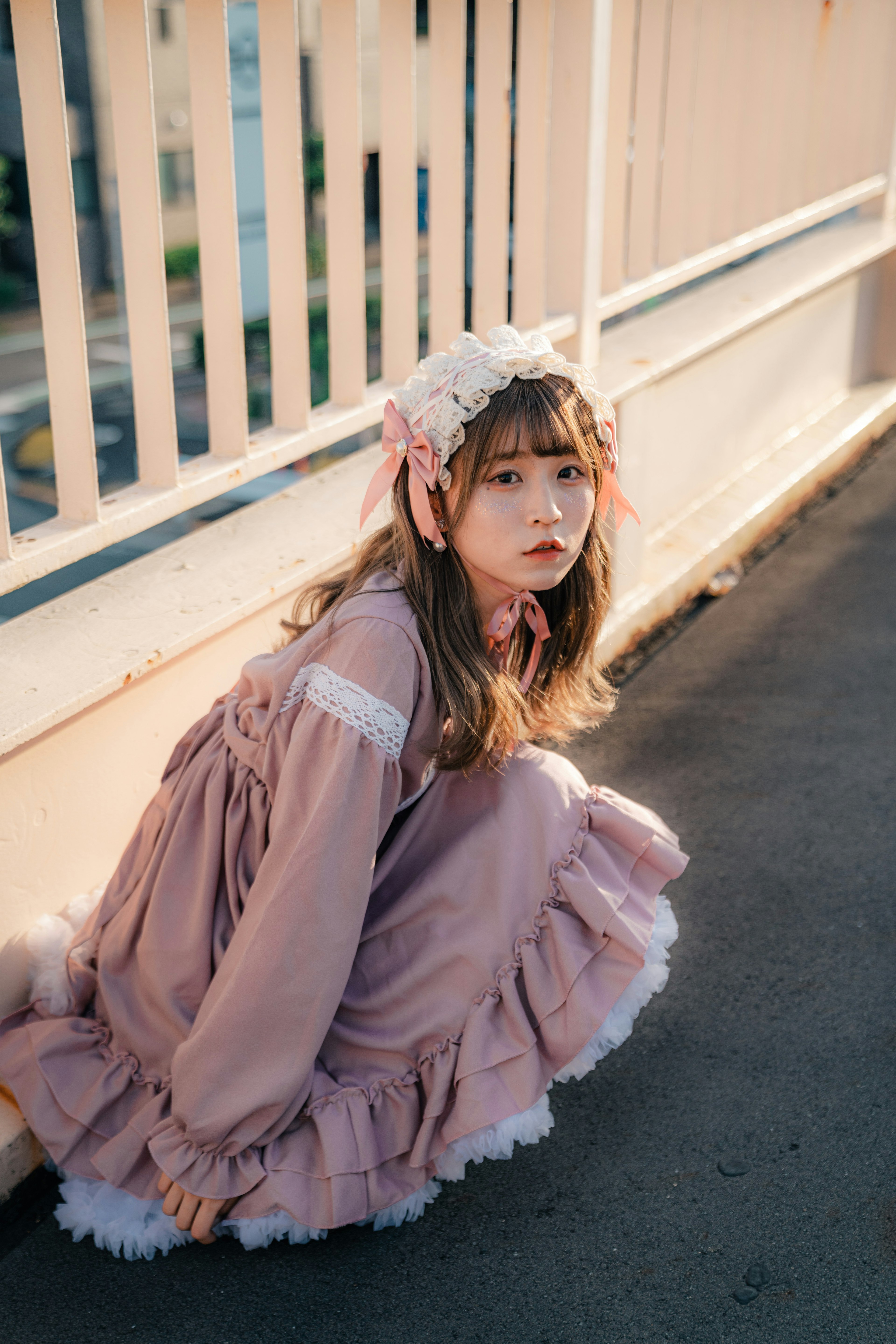 A girl wearing a pink dress sitting on the ground with a soft expression