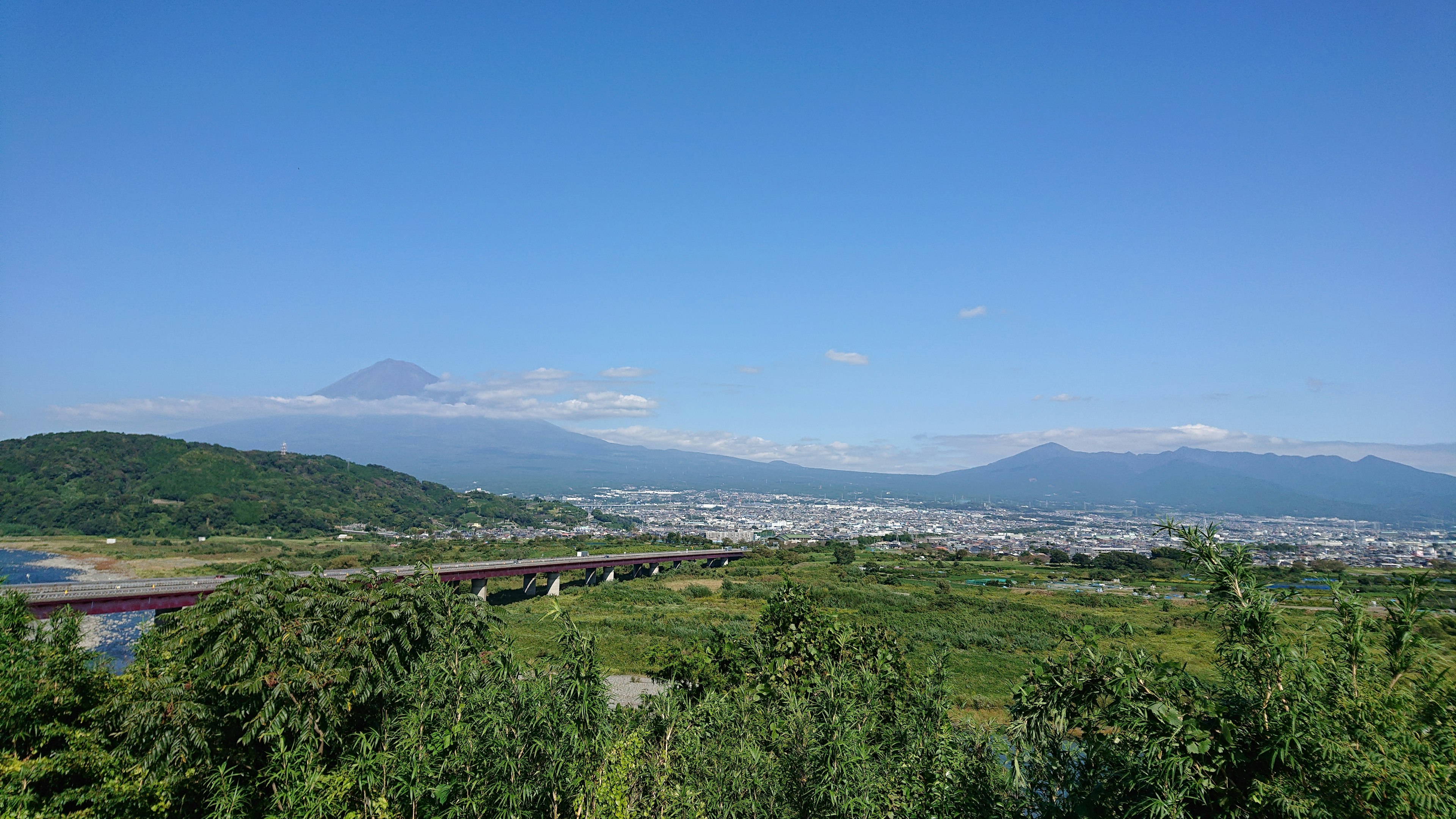 Panoramablick auf Berge und Fluss unter blauem Himmel grüne Felder und entfernte Stadt sichtbar