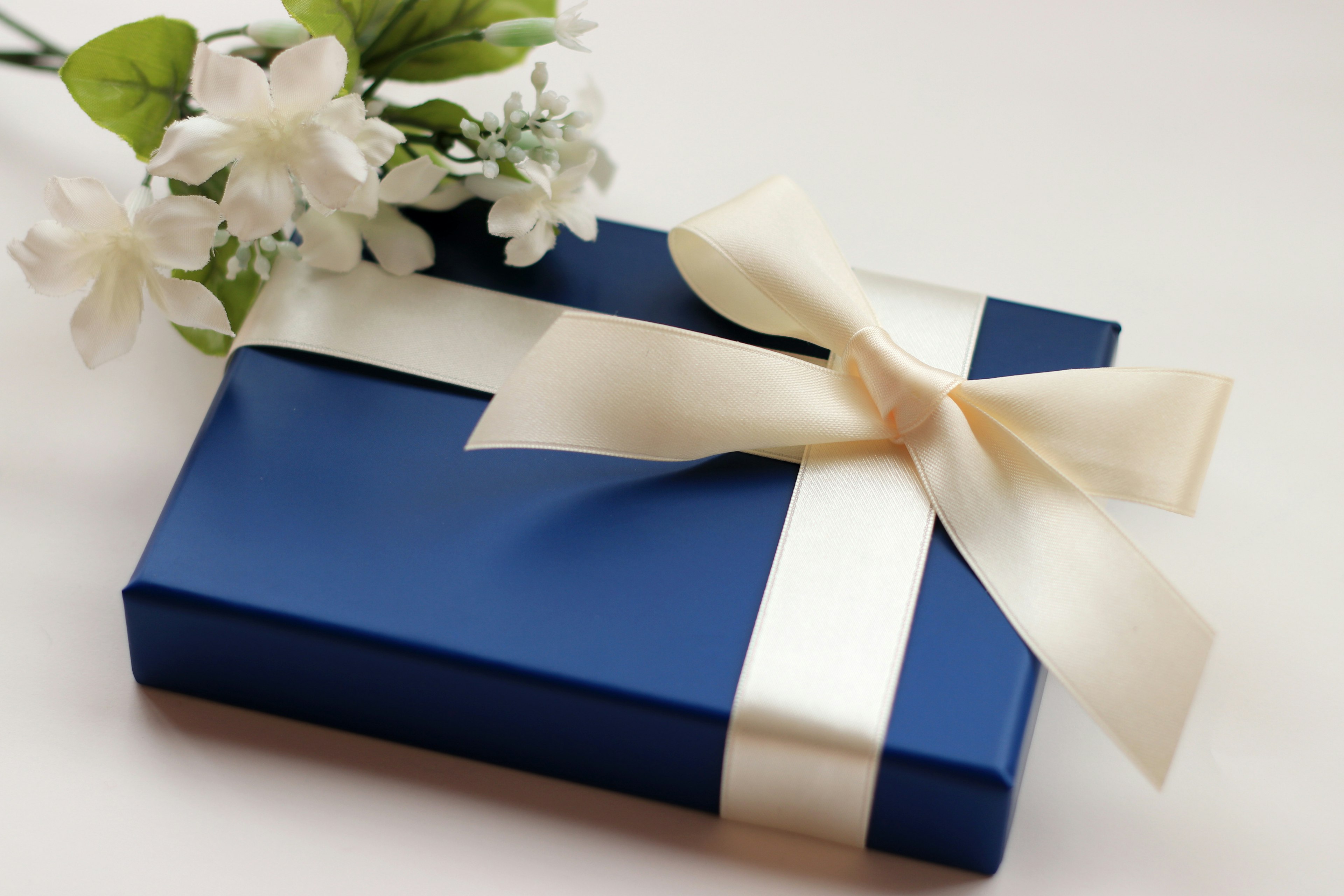 Blaue Geschenkbox mit weißem Band und Blumen