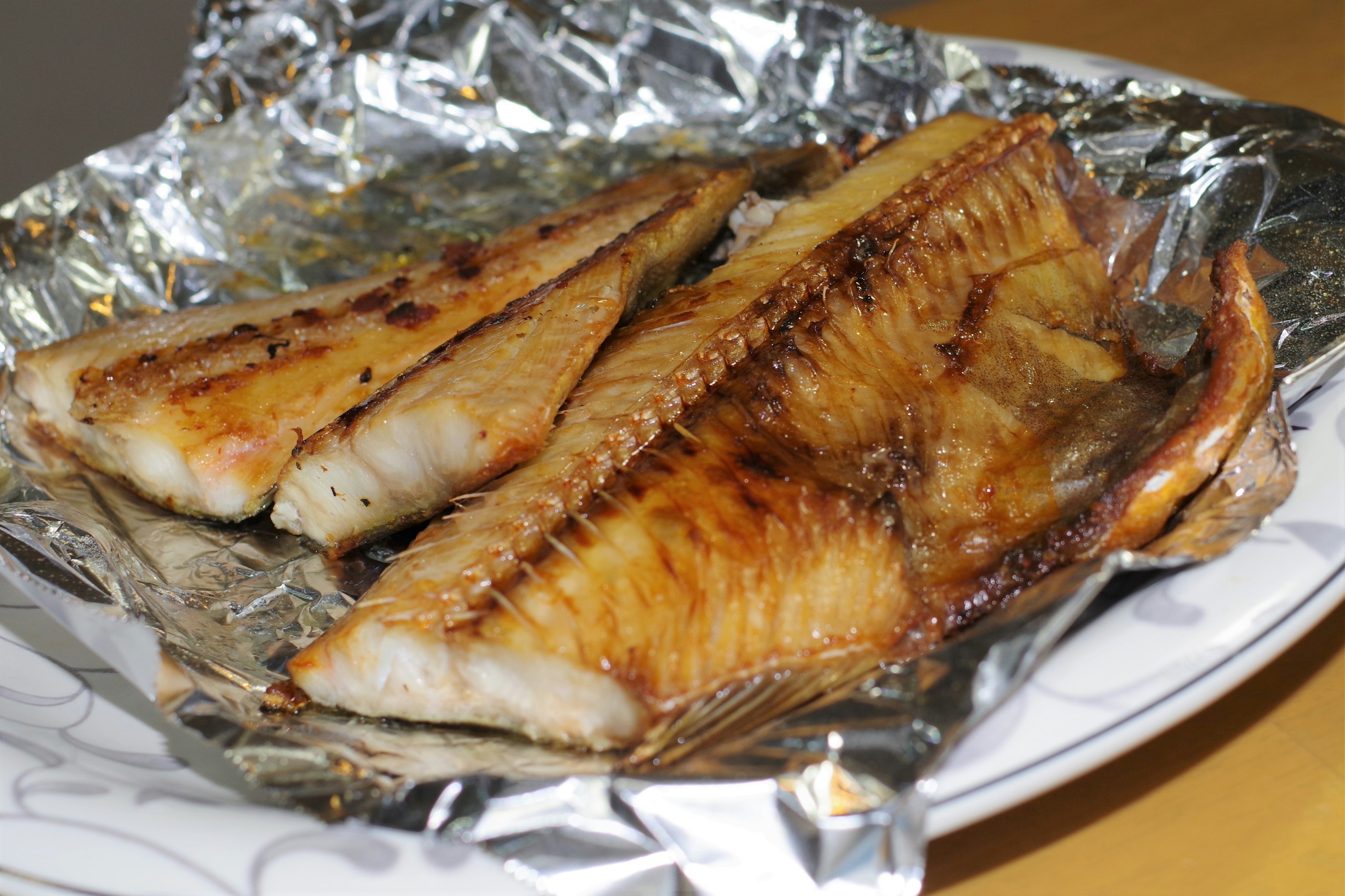 Grilled fish served on aluminum foil with a decorative plate