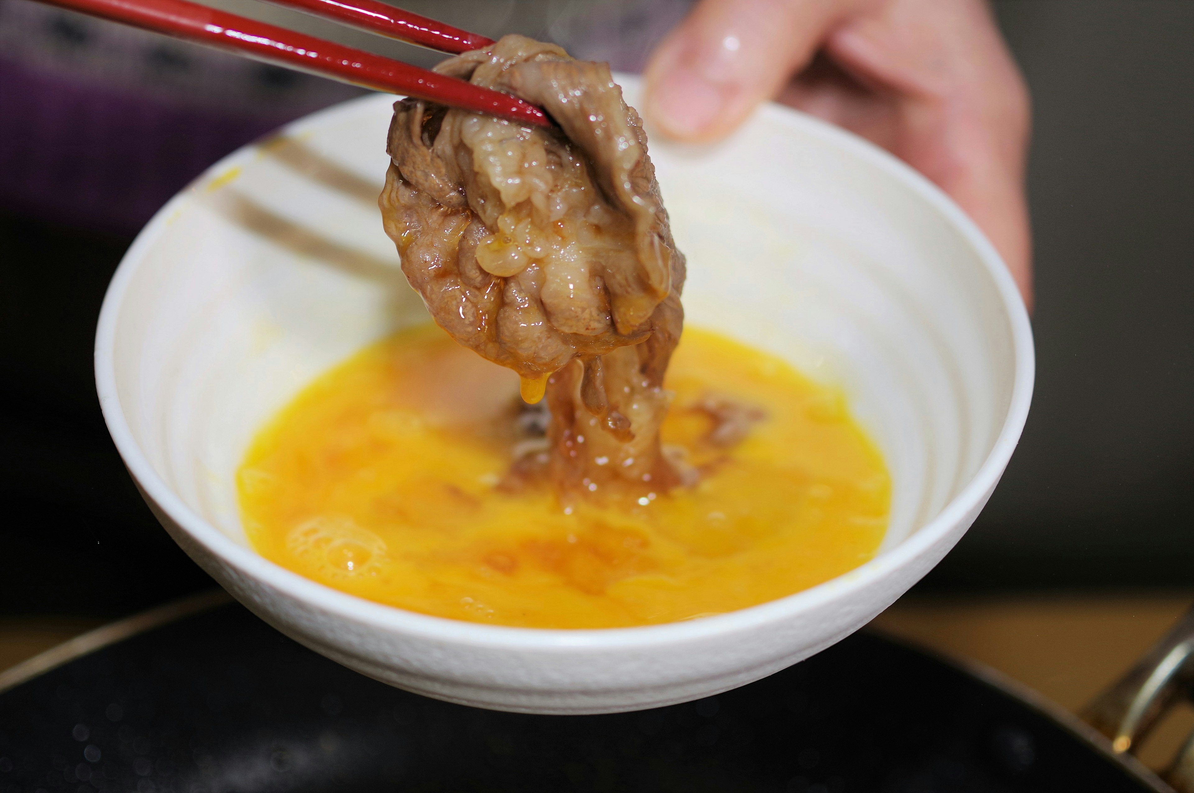 Hand mit Essstäbchen, die Fleisch in ein Ei taucht