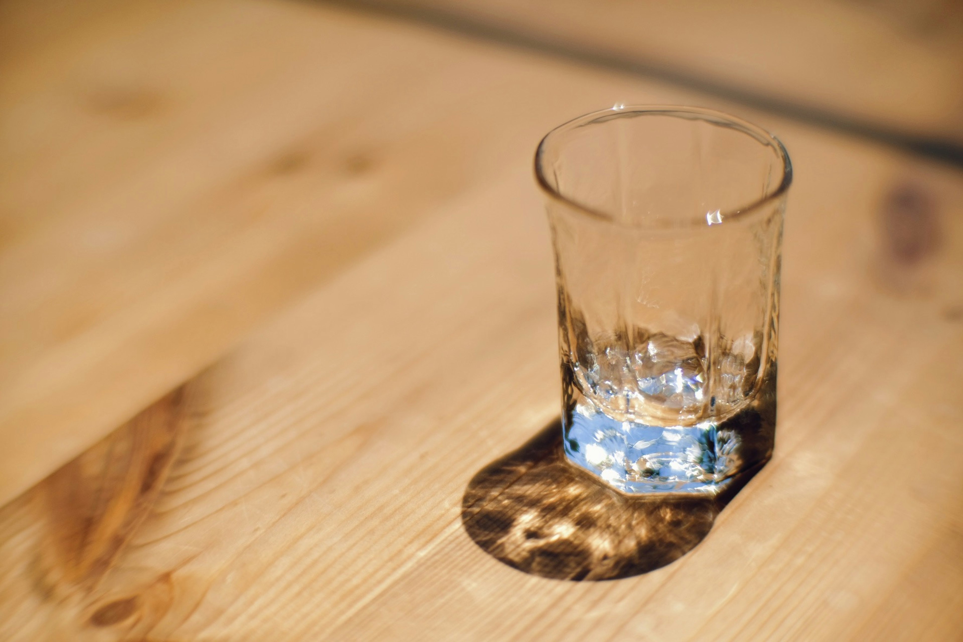 Un vaso transparente lleno de agua proyectando una sombra sobre una mesa de madera