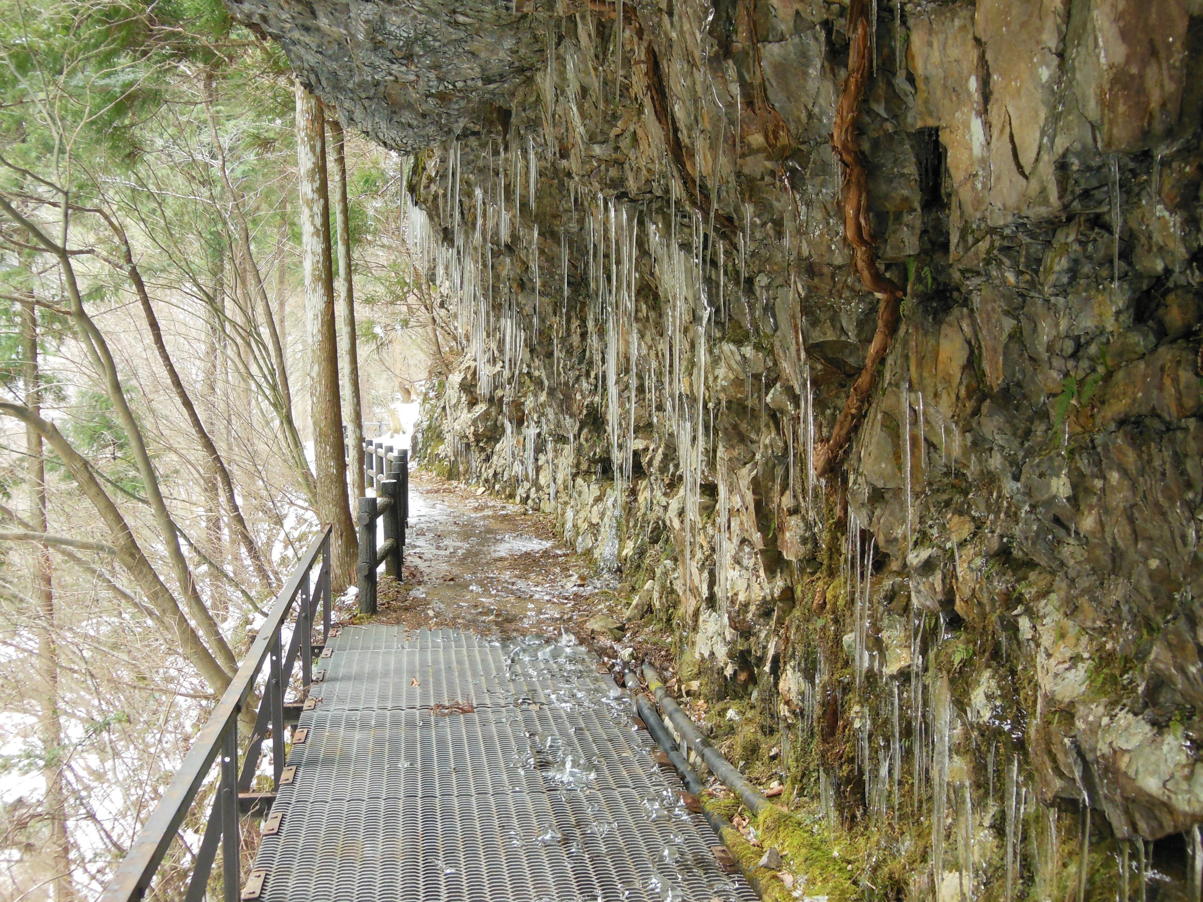 Natürlicher Weg unter einer Felsenwand mit hängenden Eiszapfen