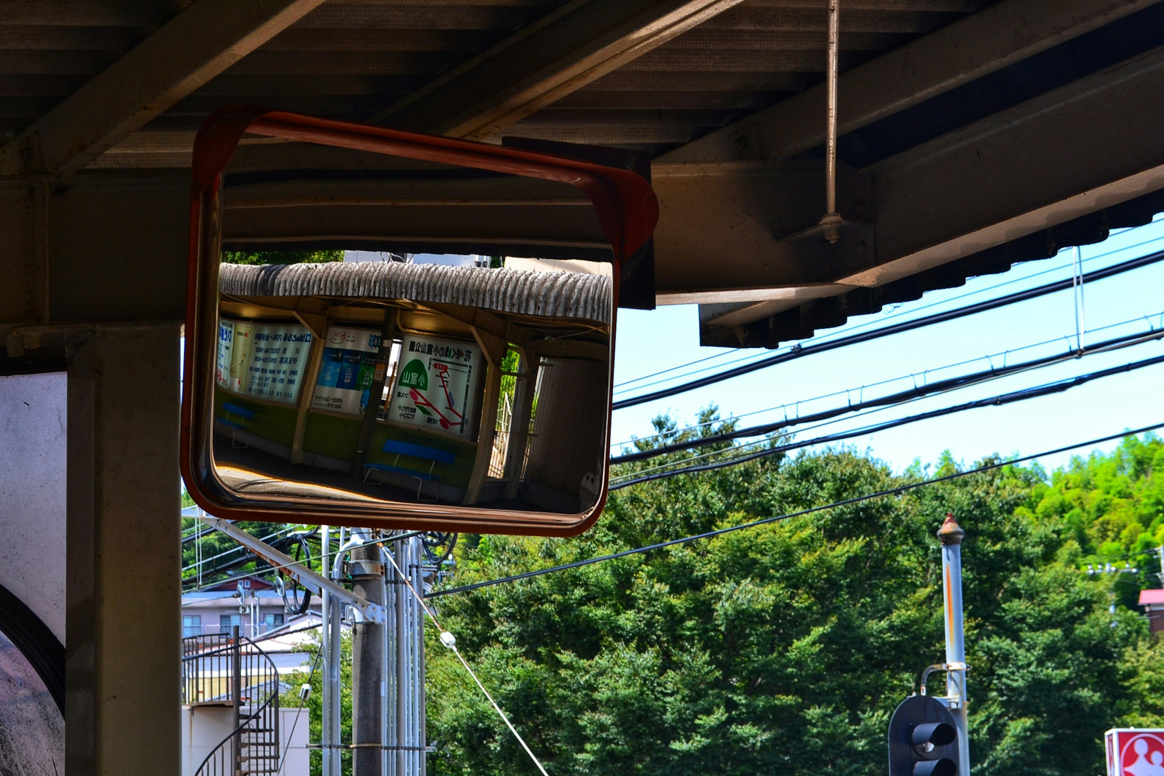 Reflexion eines Wartebereichs in einem Bahnhofsspiegel mit grünen Bäumen