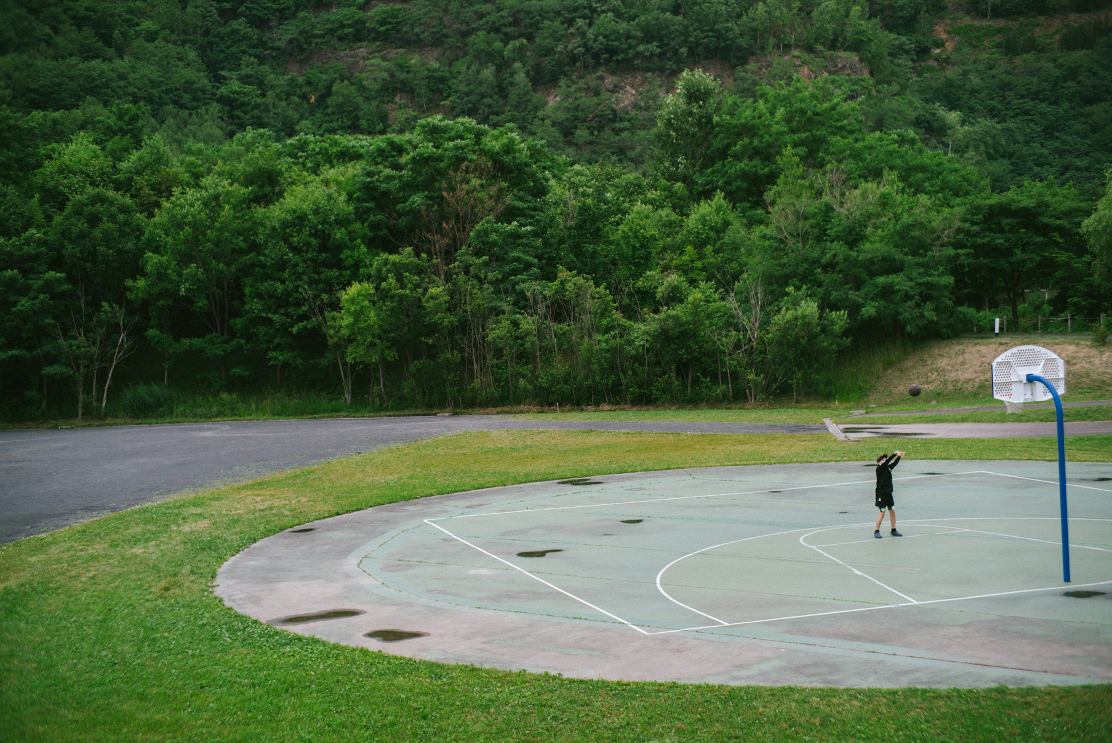 Eine Person spielt Basketball auf einem Platz, umgeben von Grün