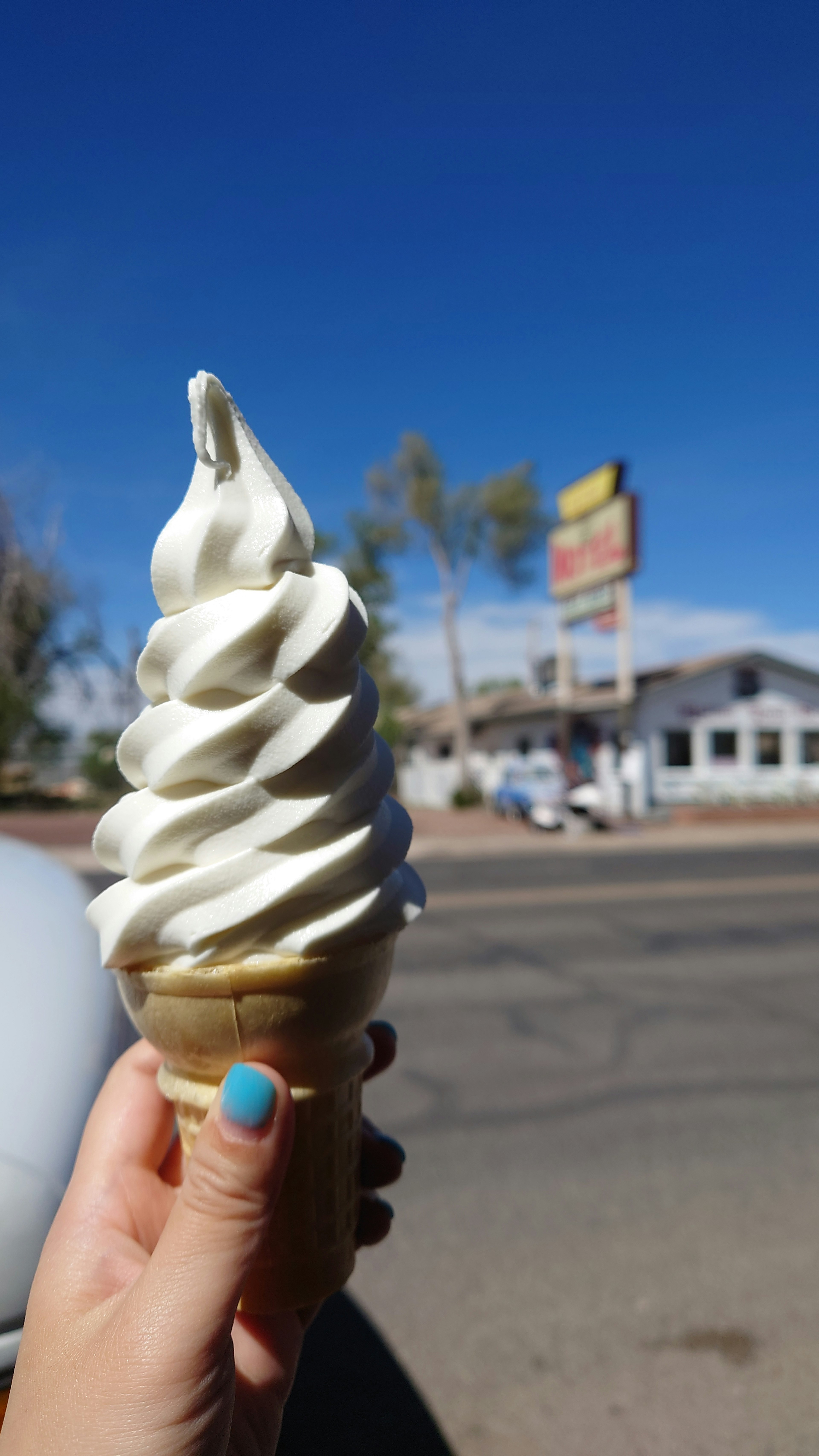 A hand holding a soft serve ice cream cone against a blue sky