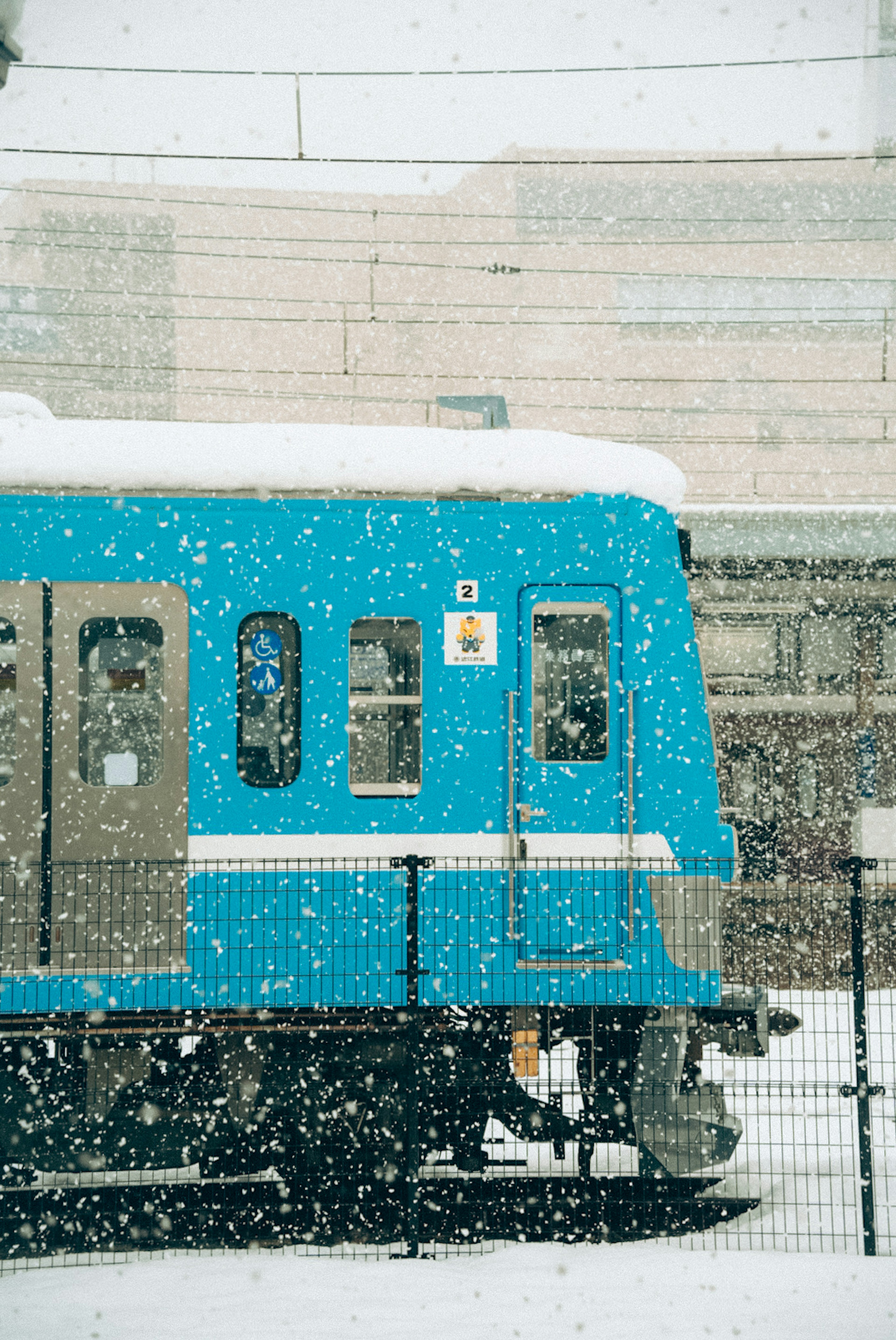 มุมมองด้านข้างของรถไฟสีน้ำเงินในหิมะโดยมีอาคารอยู่ในพื้นหลัง