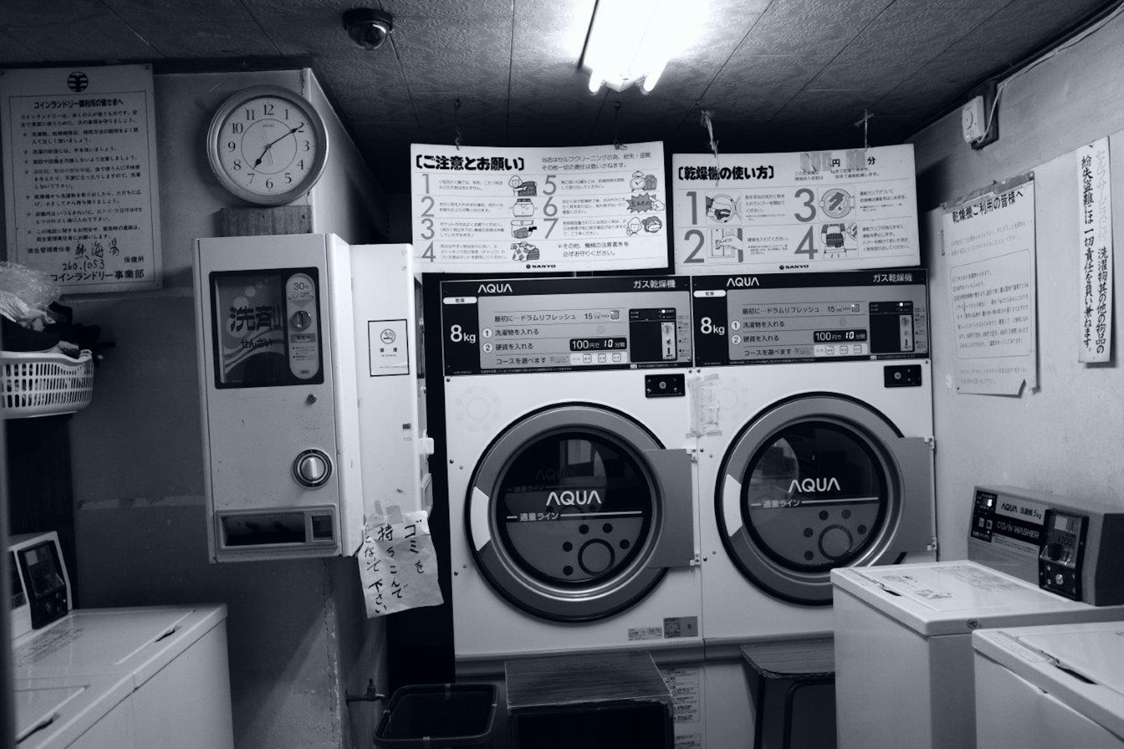 Black and white laundry room with two washing machines a clock and instruction sheets on the wall